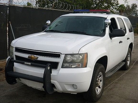 a white suv with a police light on top of it is parked in front of a barbed wire fence  and ready to install a pod rig for film shooting.