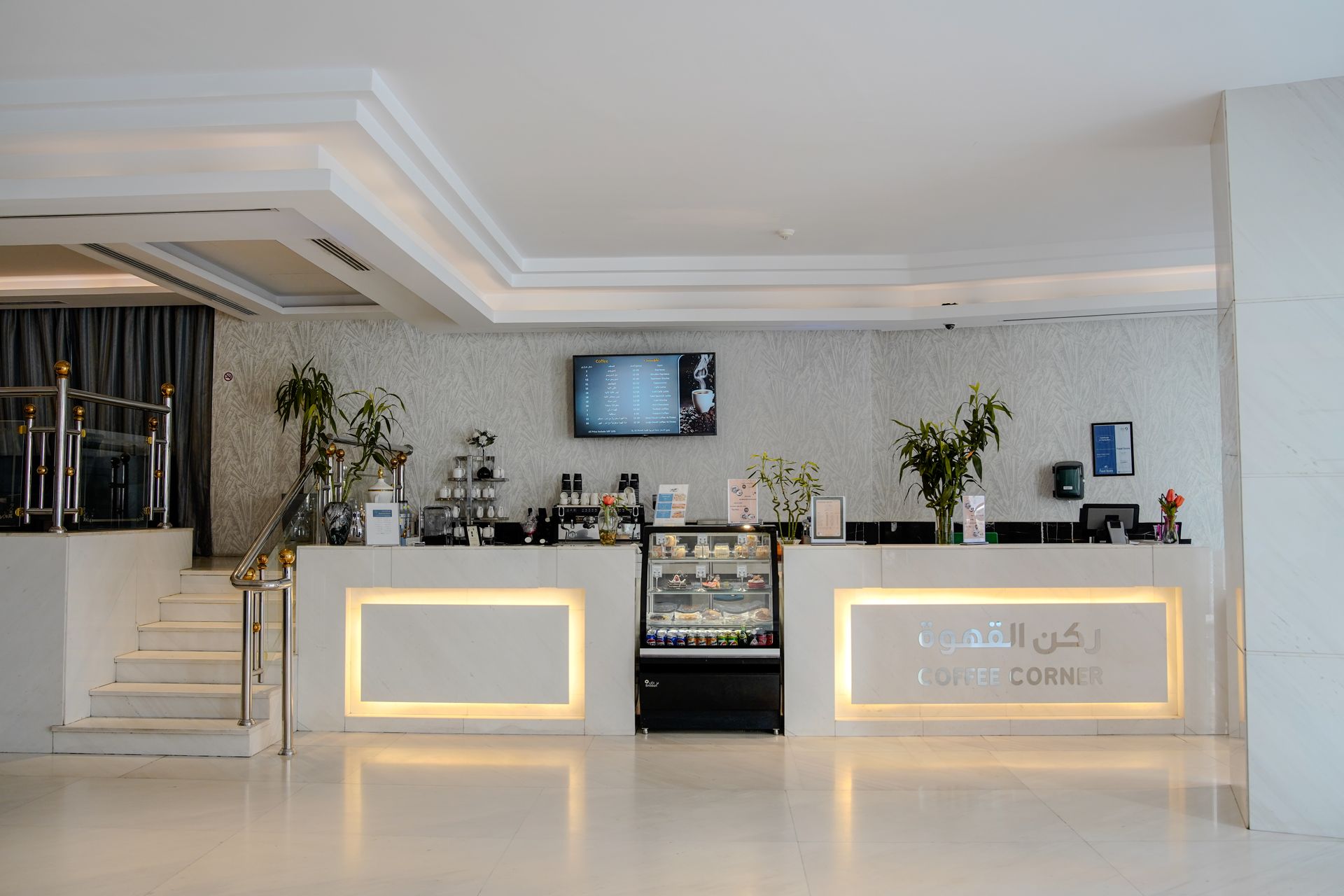 Modern hotel reception desk with illuminated counters, marble floor, and wall-mounted TV in a bright lobby