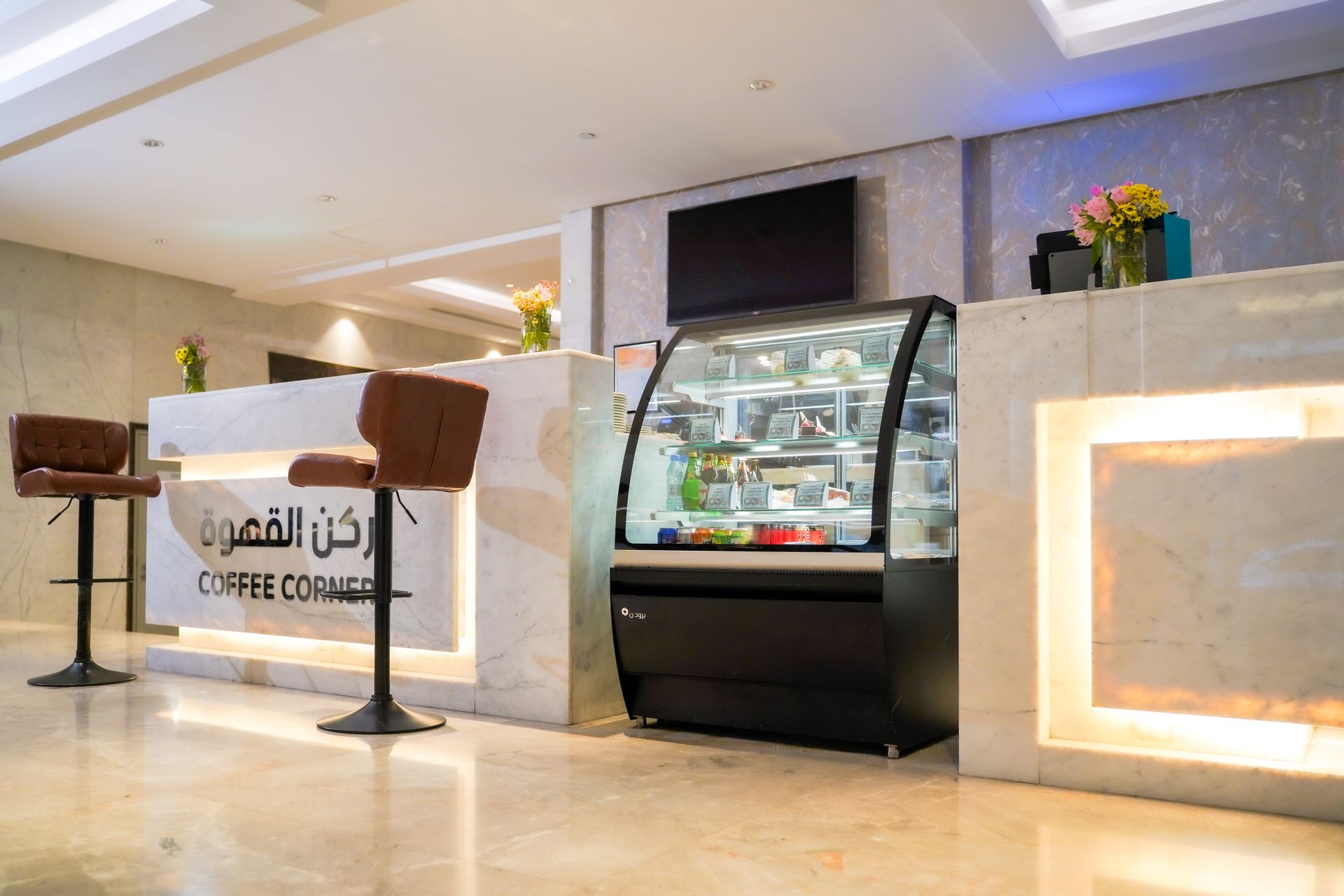 Modern coffee counter with a display fridge and Arabic signage in a bright café interior
