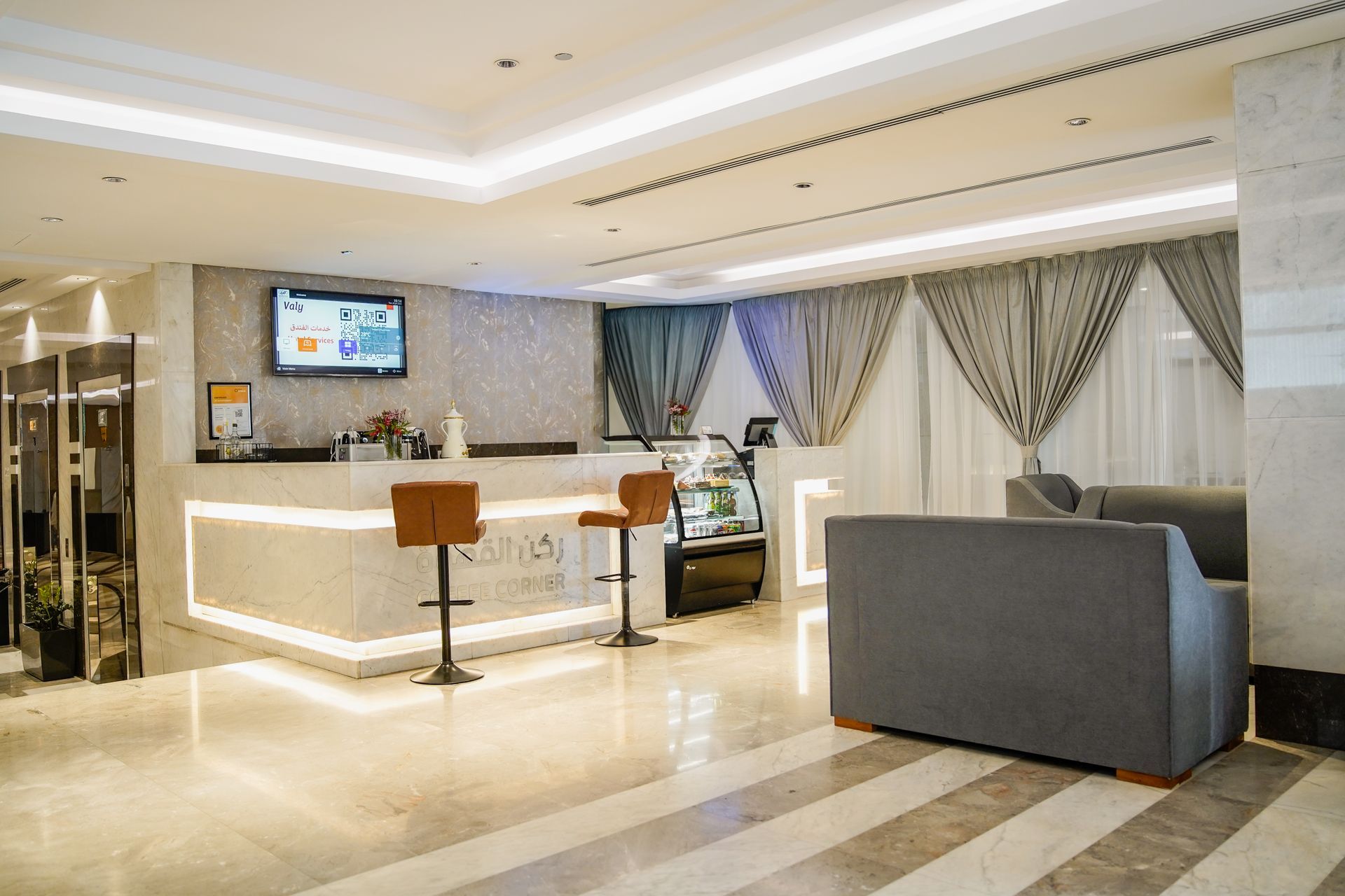 Modern hotel lobby with white reception desk, gray seating, and wall-mounted TV