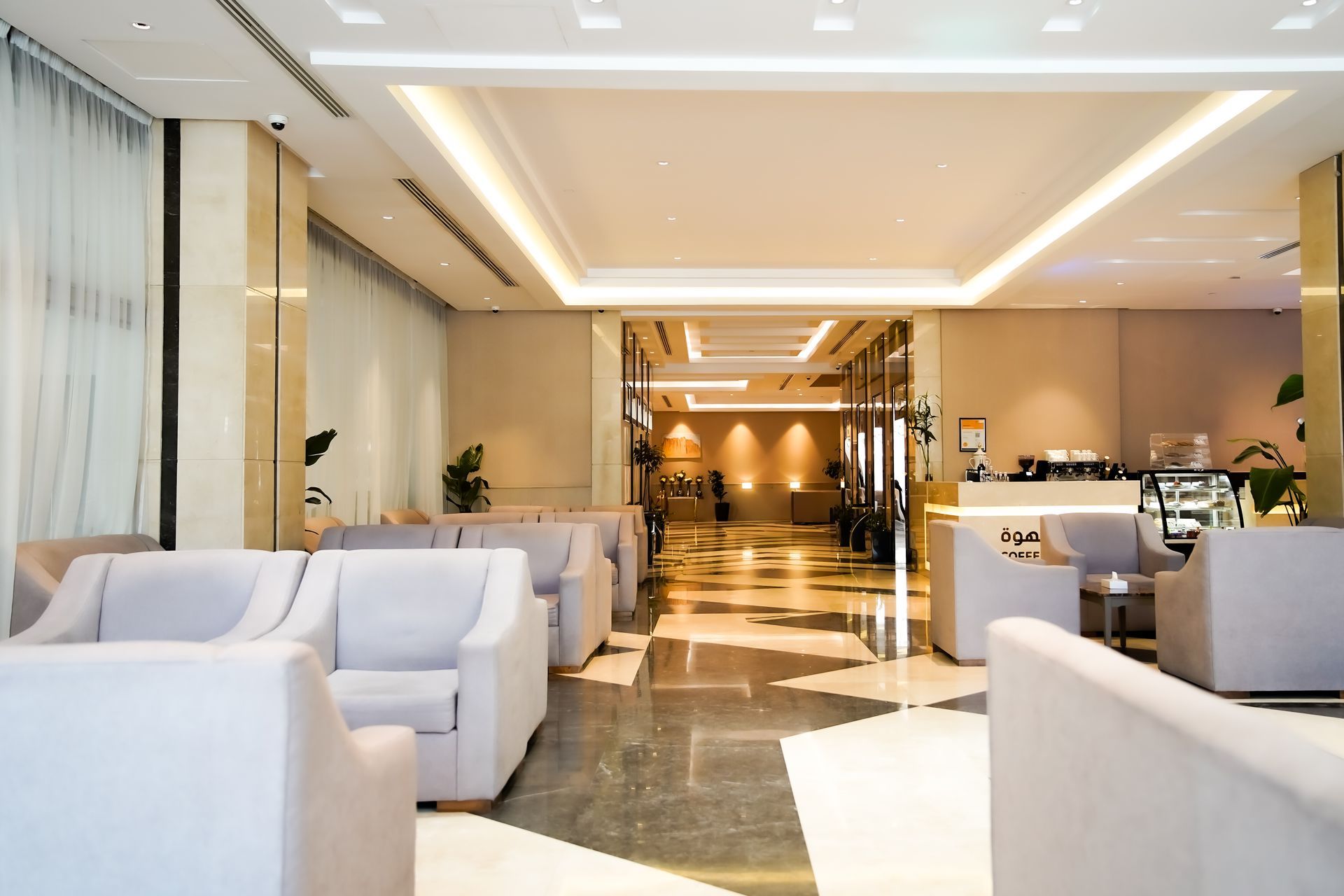 Modern hotel lounge with white sofas, polished floors, and warm lighting leading to a reception area