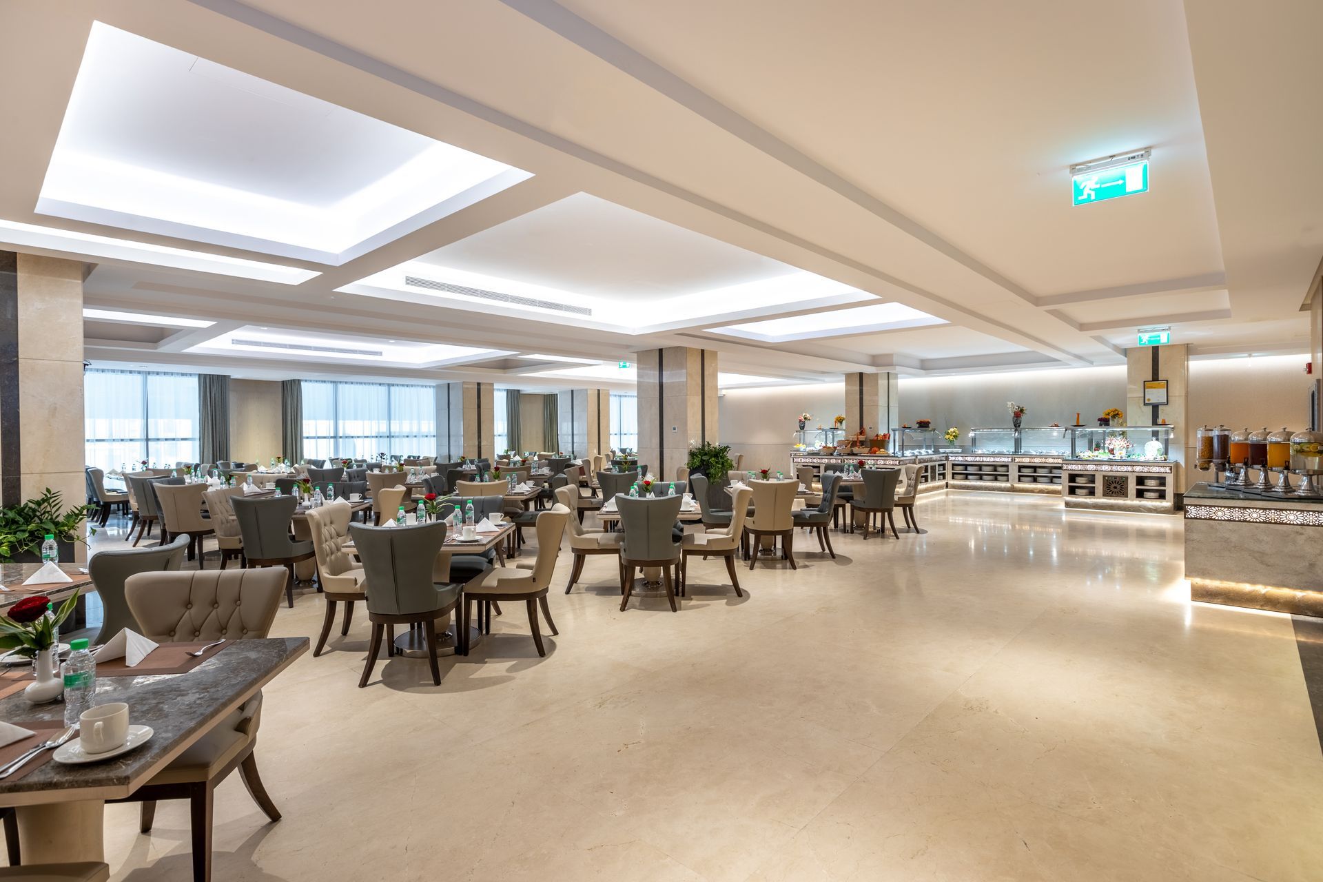 Bright modern hotel restaurant with empty tables, chairs, and large windows overlooking the city.