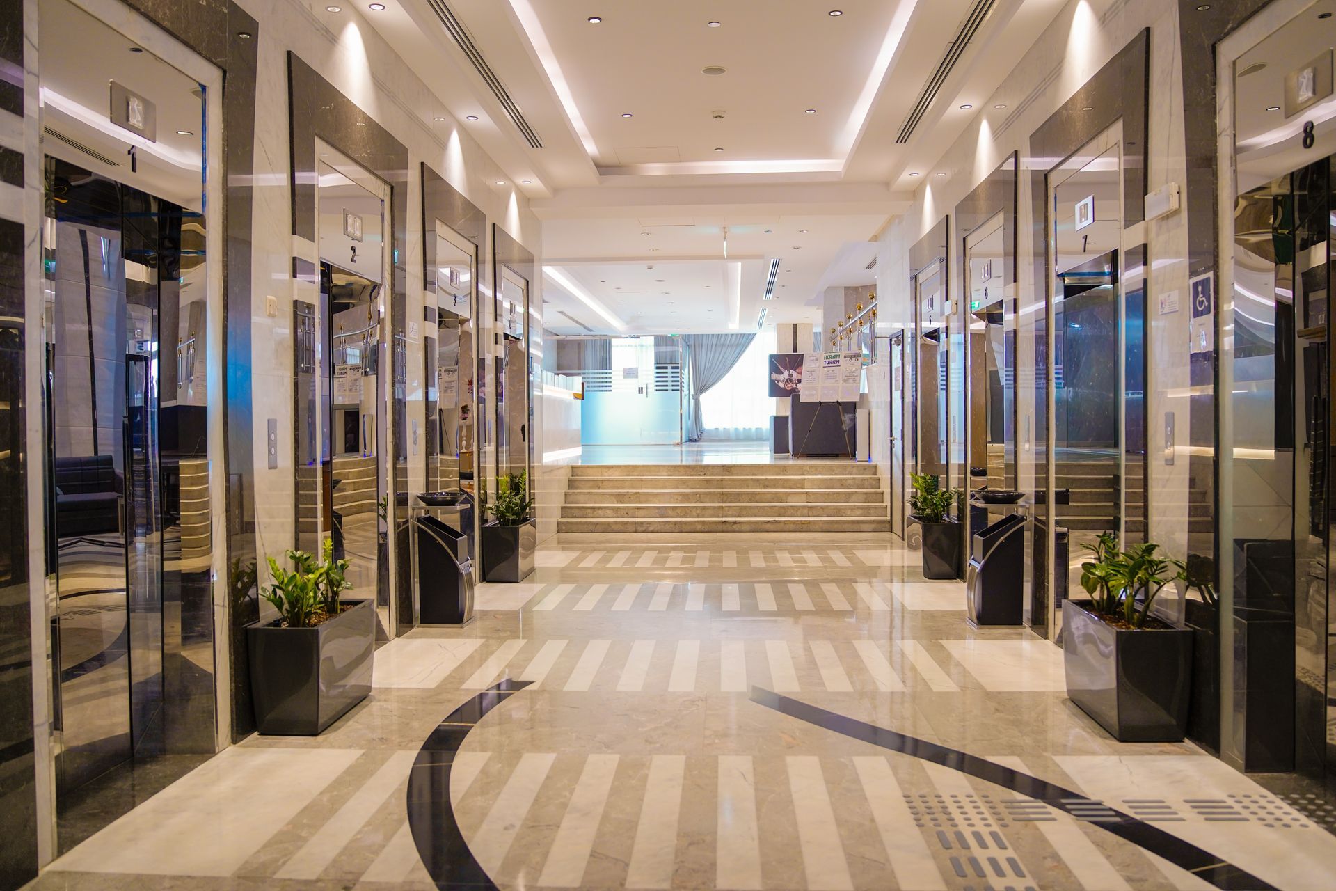 Bright indoor shopping mall corridor with glass storefronts and striped carpet leading to stairs