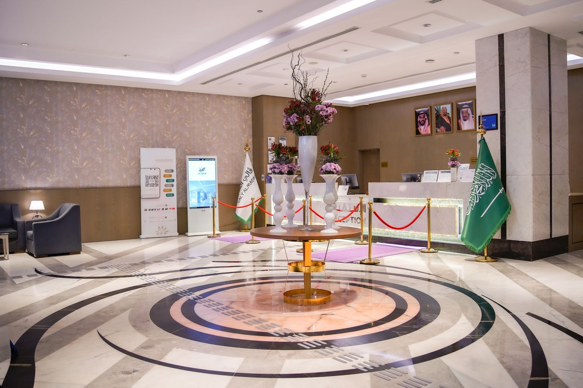 Elegant lobby with circular marble floor design, floral display, and flags near a reception area