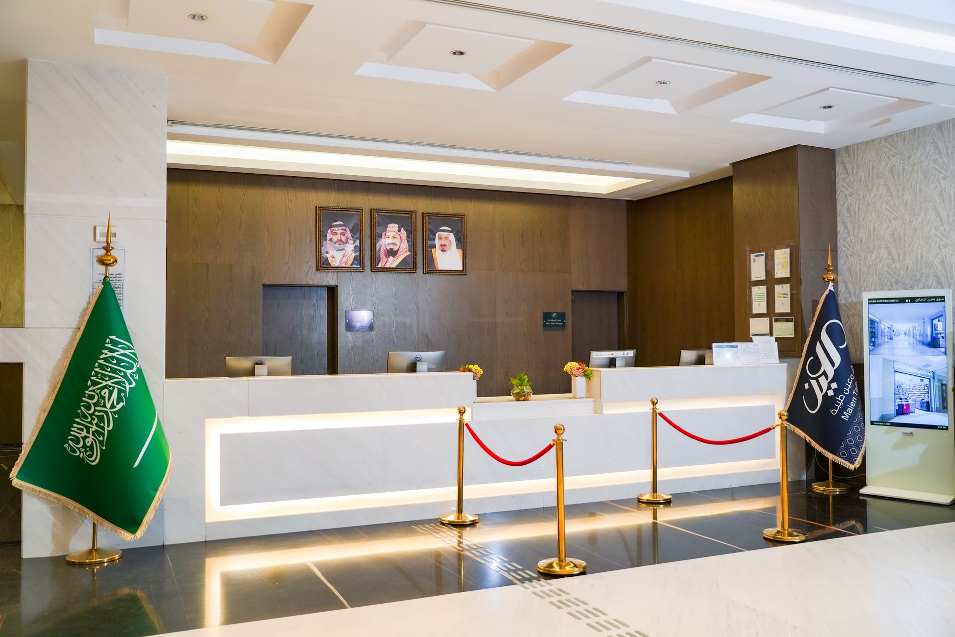 Modern hotel reception desk with Saudi flags and framed portraits on the wall
