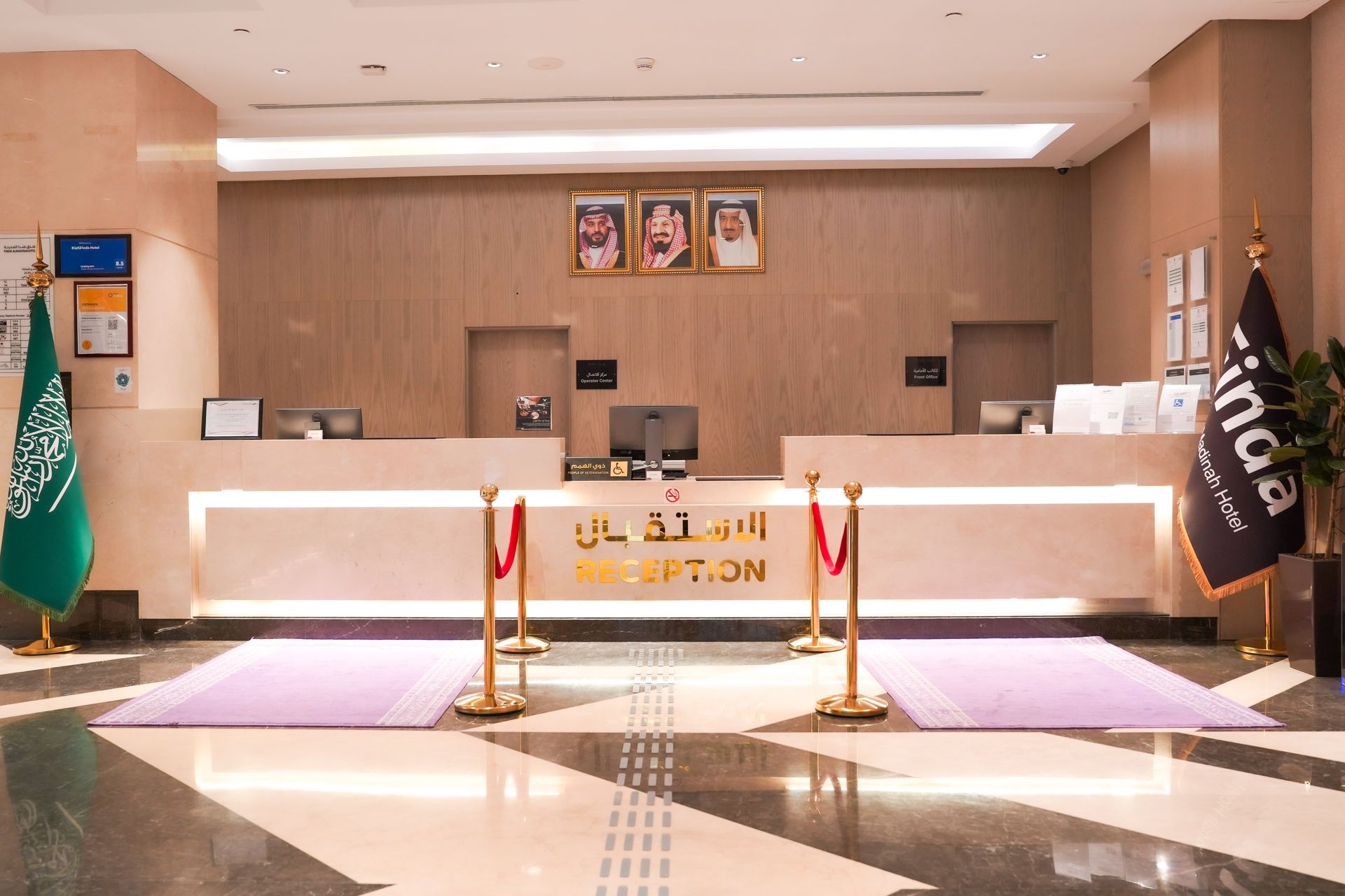 Hotel reception desk with Saudi flags, purple carpet, and beige lobby interior