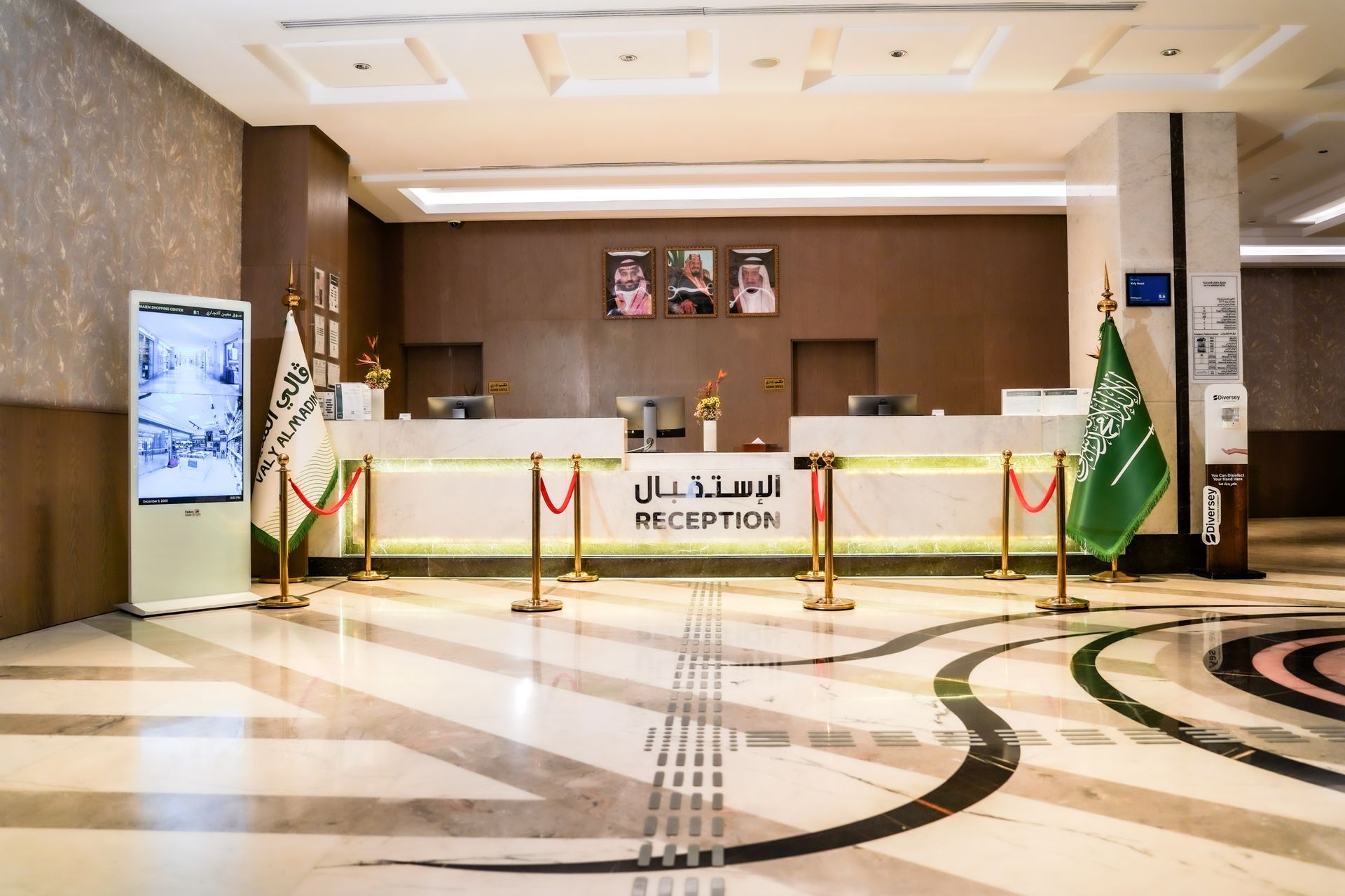 Hotel lobby reception desk with Arabic signage, marble floor, and decorative plants