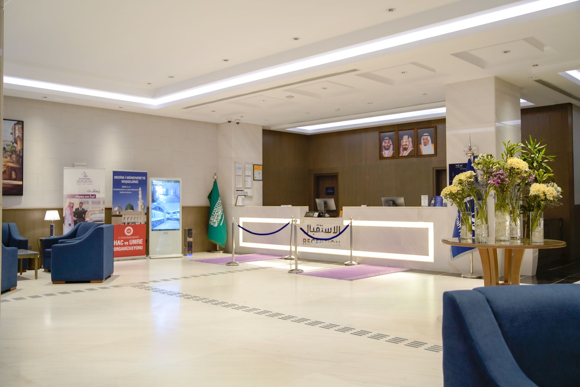 Hotel lobby with reception desk, blue seating, and floral arrangements