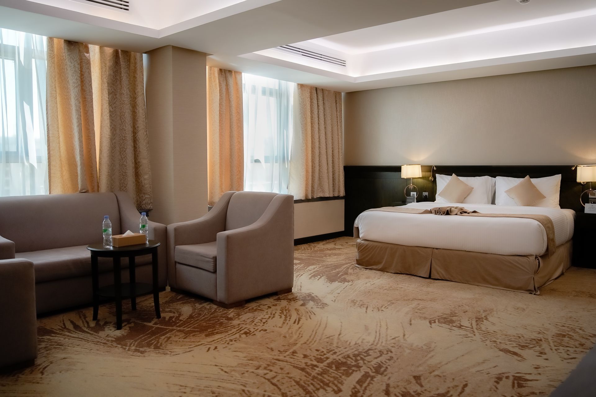 Hotel room with bed, armchairs, table, lamp, and beige decor