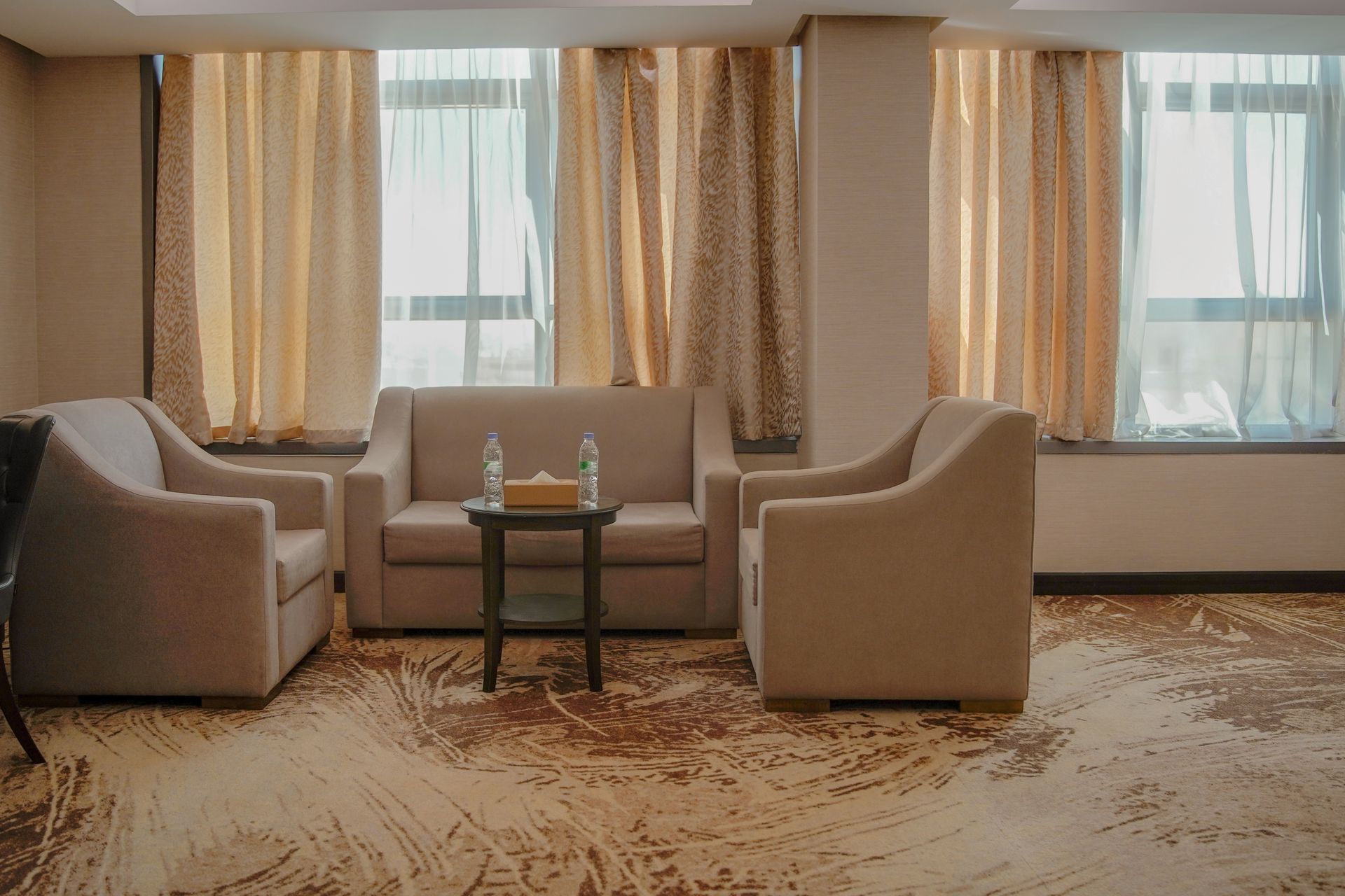 Modern hotel lounge with beige sofas, curtains, and a small table by large windows