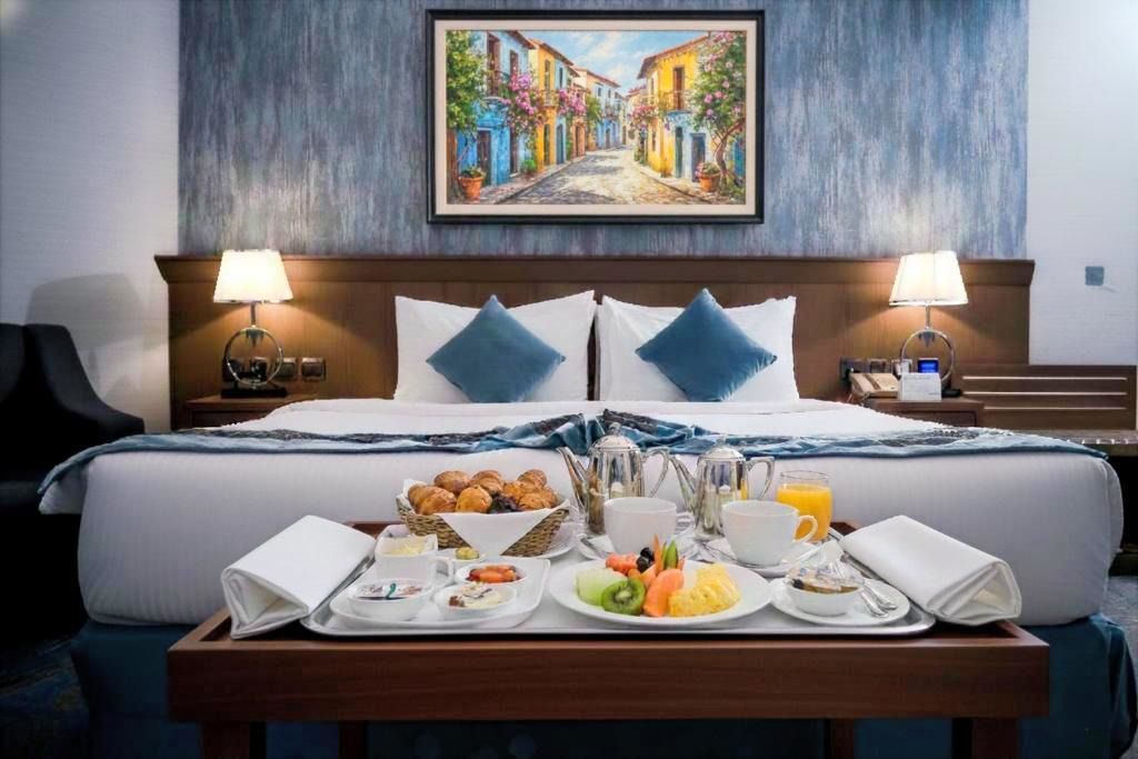 Hotel room with neatly made bed, breakfast tray on table, and framed artwork above the headboard