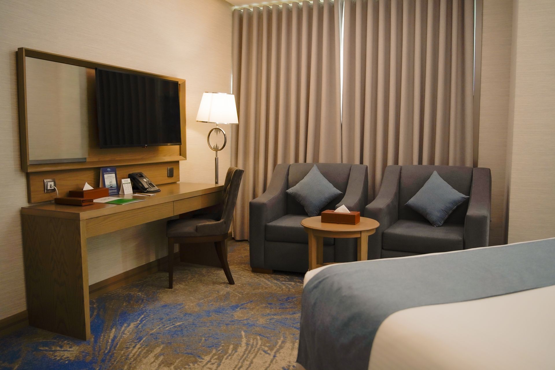 Hotel room with desk, chair, sofa, lamp, and bed beside closed curtains