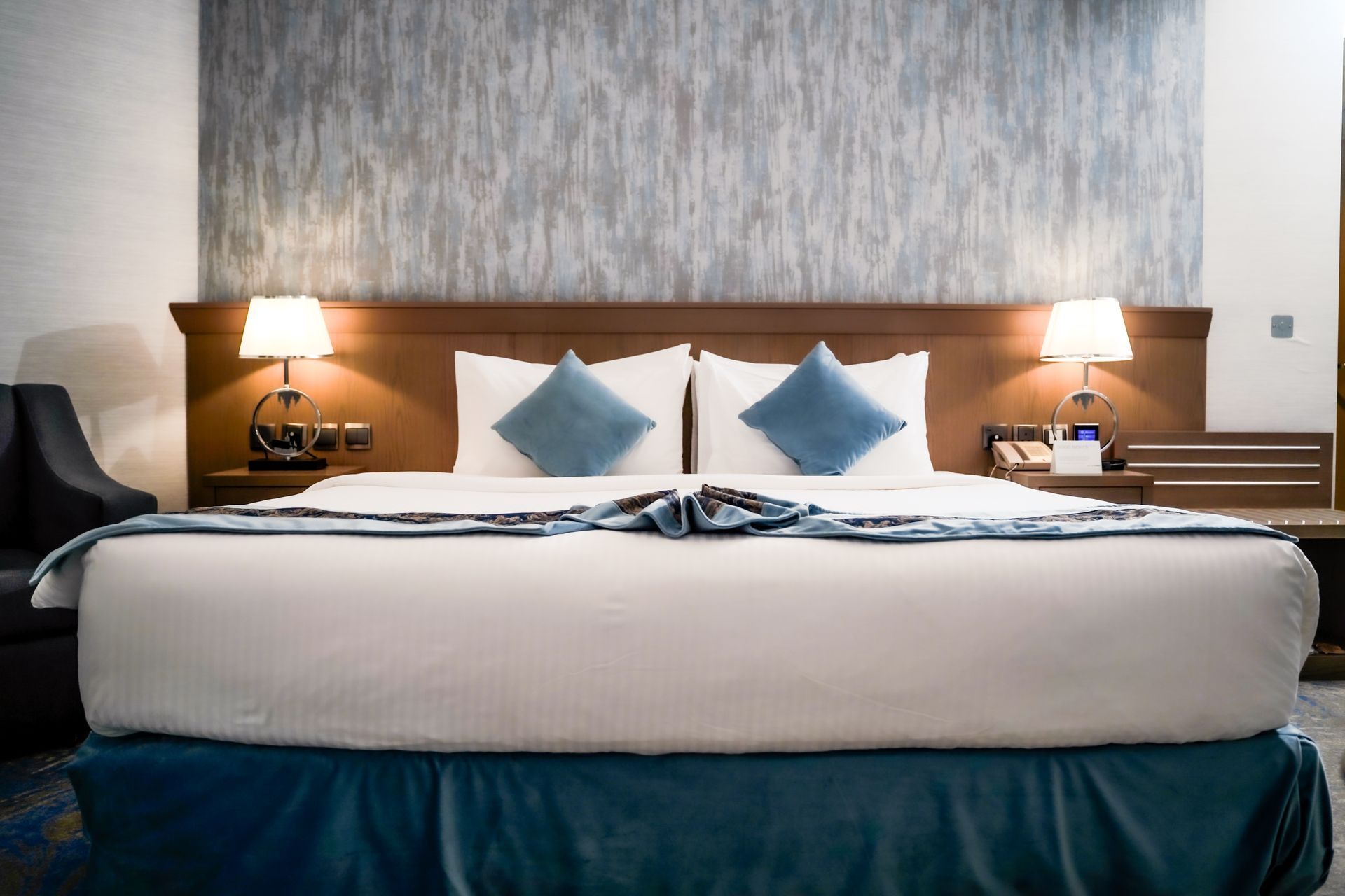 Hotel room with a neatly made bed, blue accents, and two lit bedside lamps