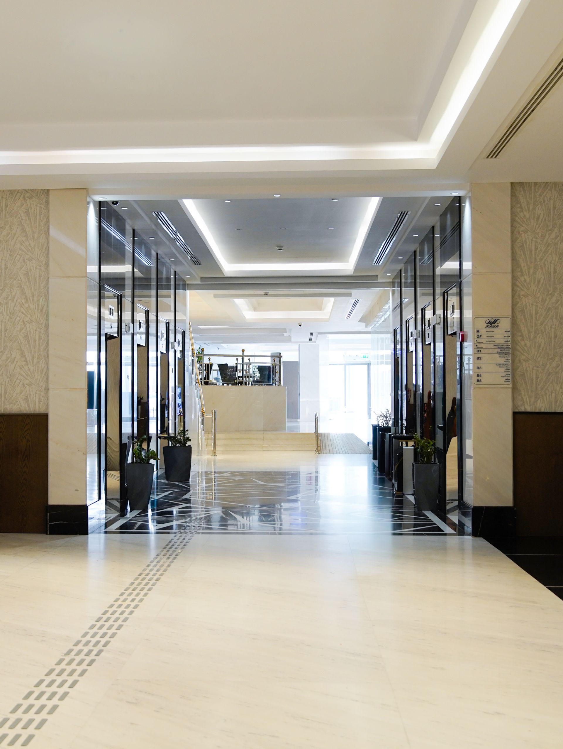 Bright mall corridor with reflective floor, glass storefronts, and beige ceiling lighting