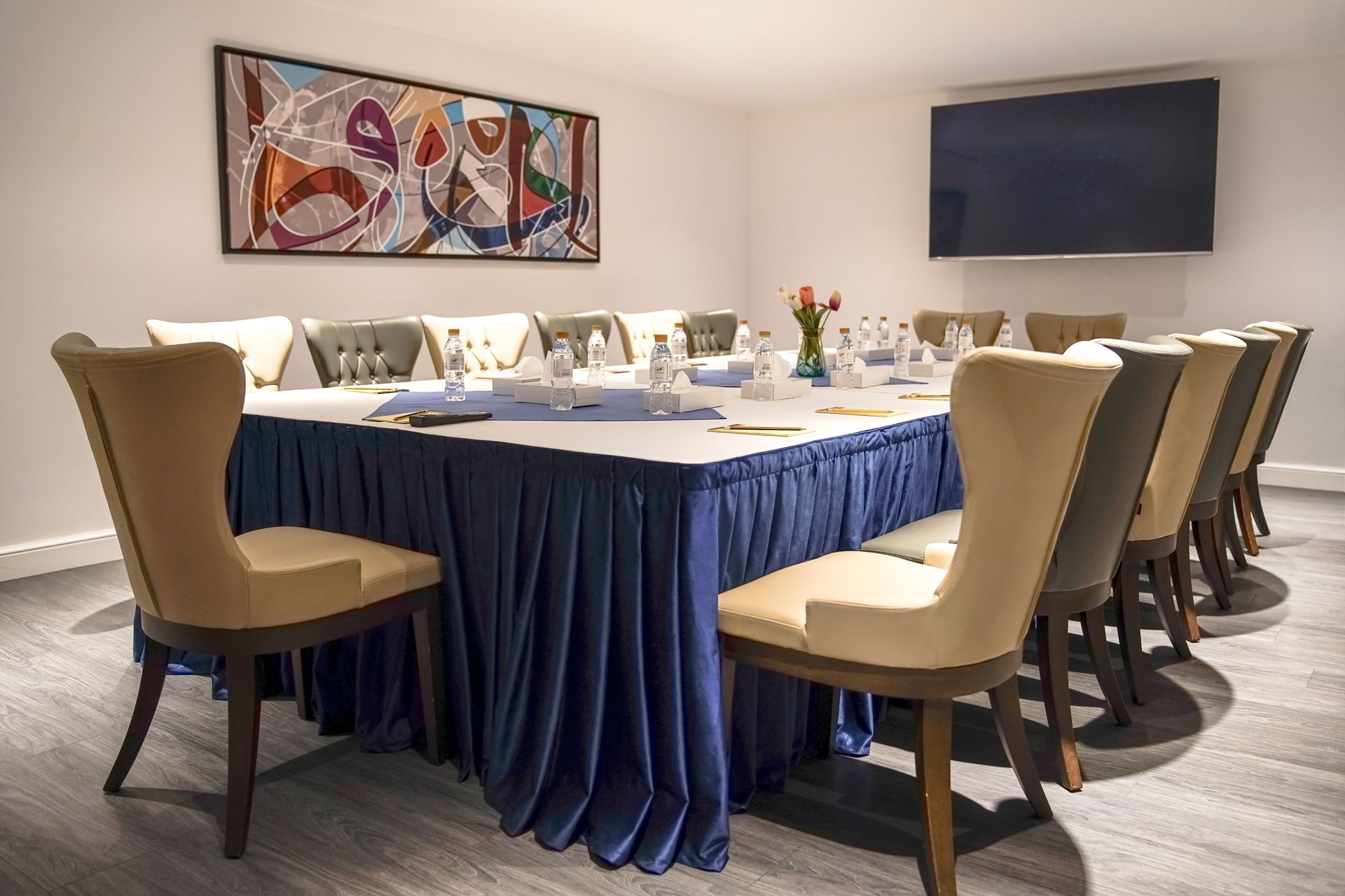 Conference room with a long blue-draped table, beige chairs, and wall art under soft lighting