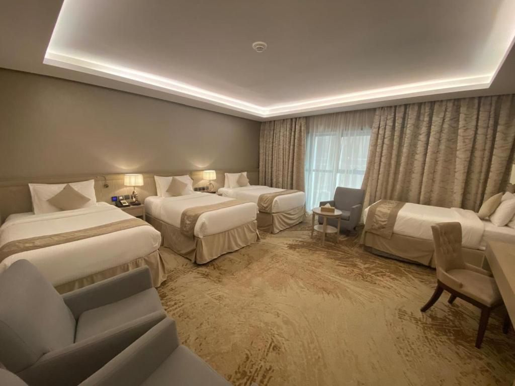 Spacious hotel room with three beds, armchairs, and a window with curtains.