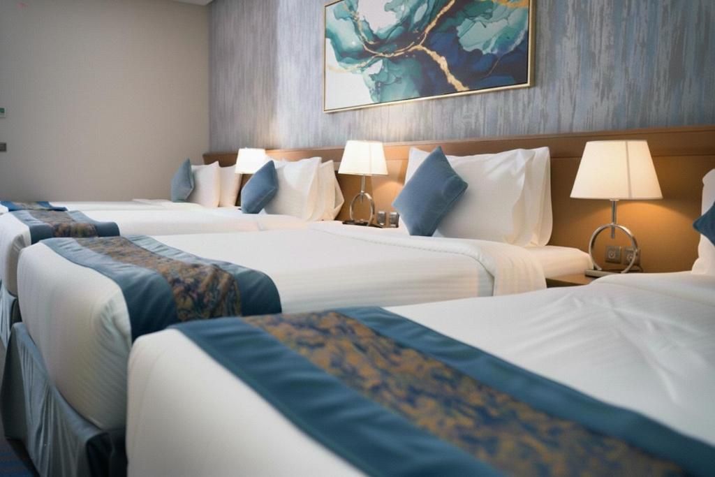 Hotel room with two neatly made beds, blue accents, bedside lamp, and wall art