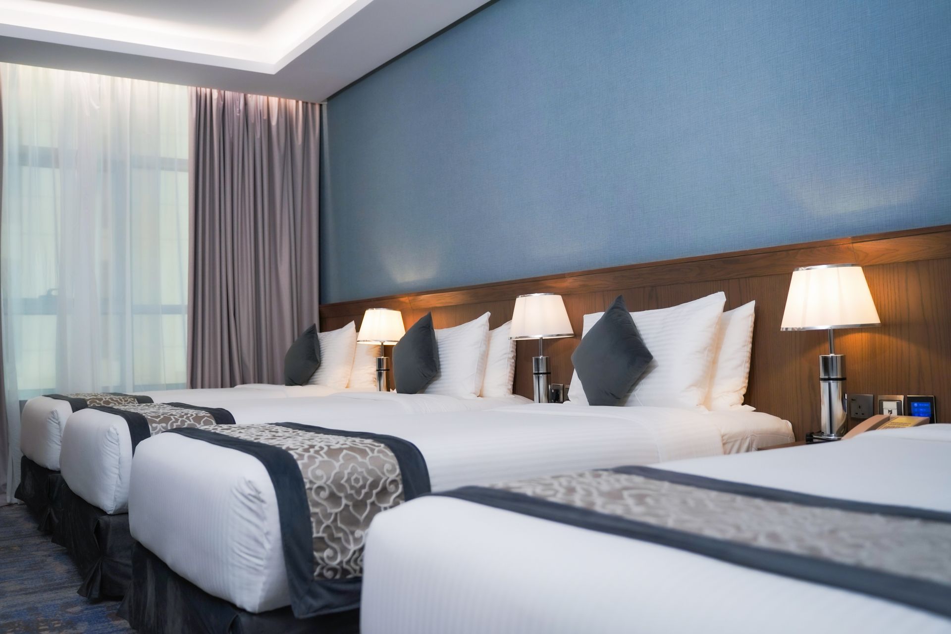 Modern hotel room with neatly made twin beds, blue accent wall, and soft bedside lamps