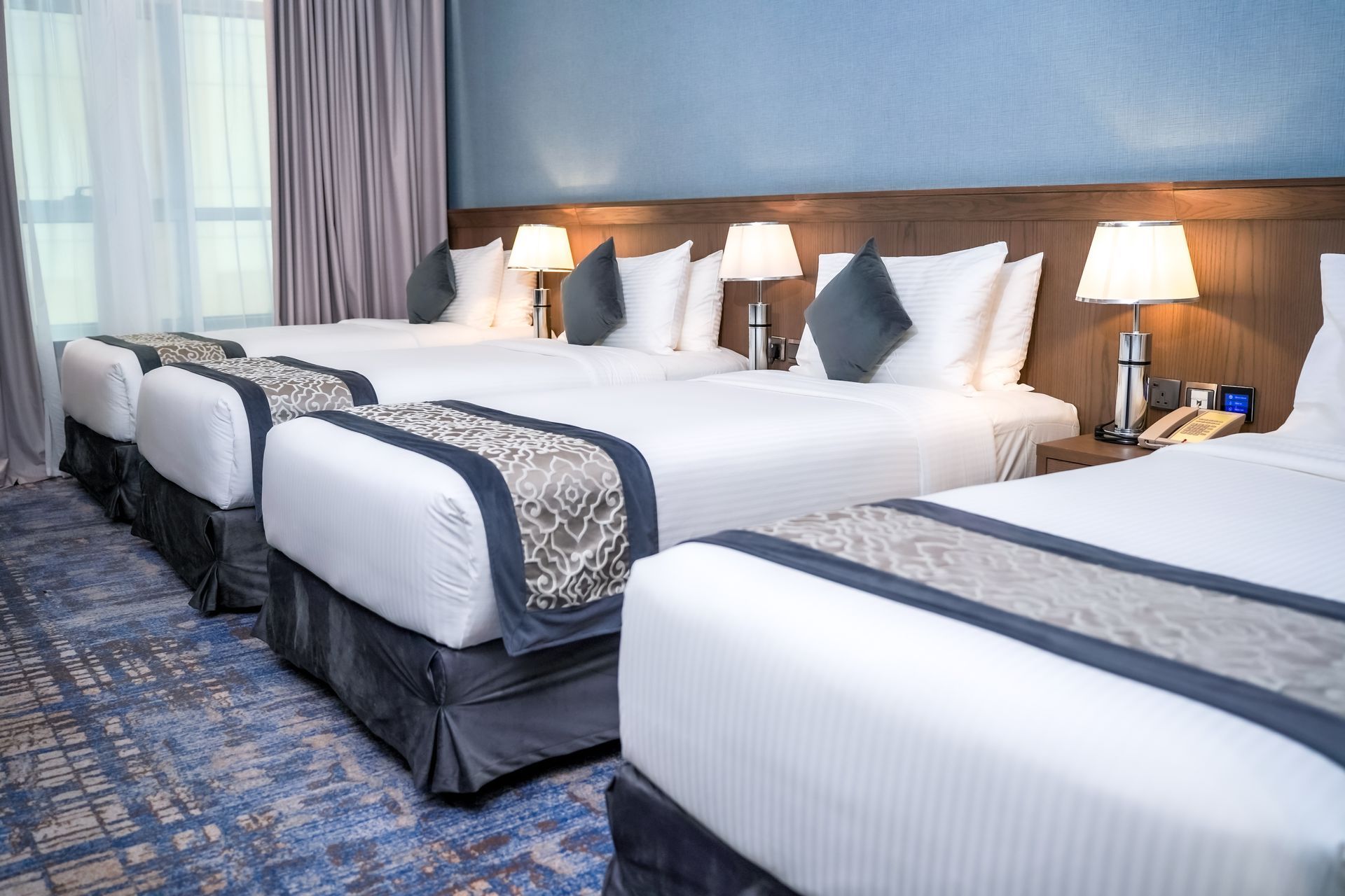 Hotel room with several neatly made twin beds, blue carpet, and warm bedside lamps