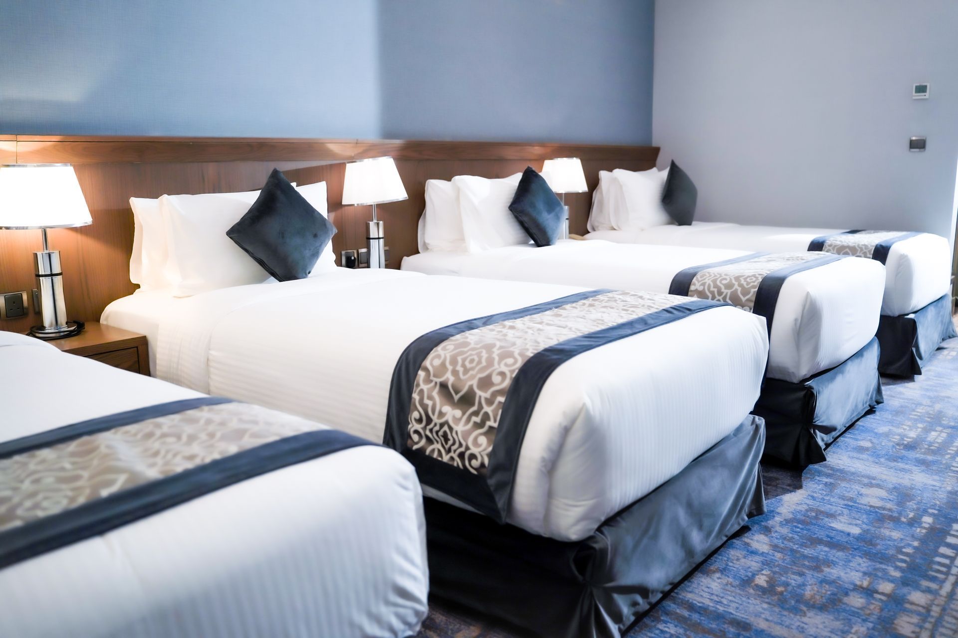 Hotel room with four neatly made beds, bedside lamps, and blue patterned carpet