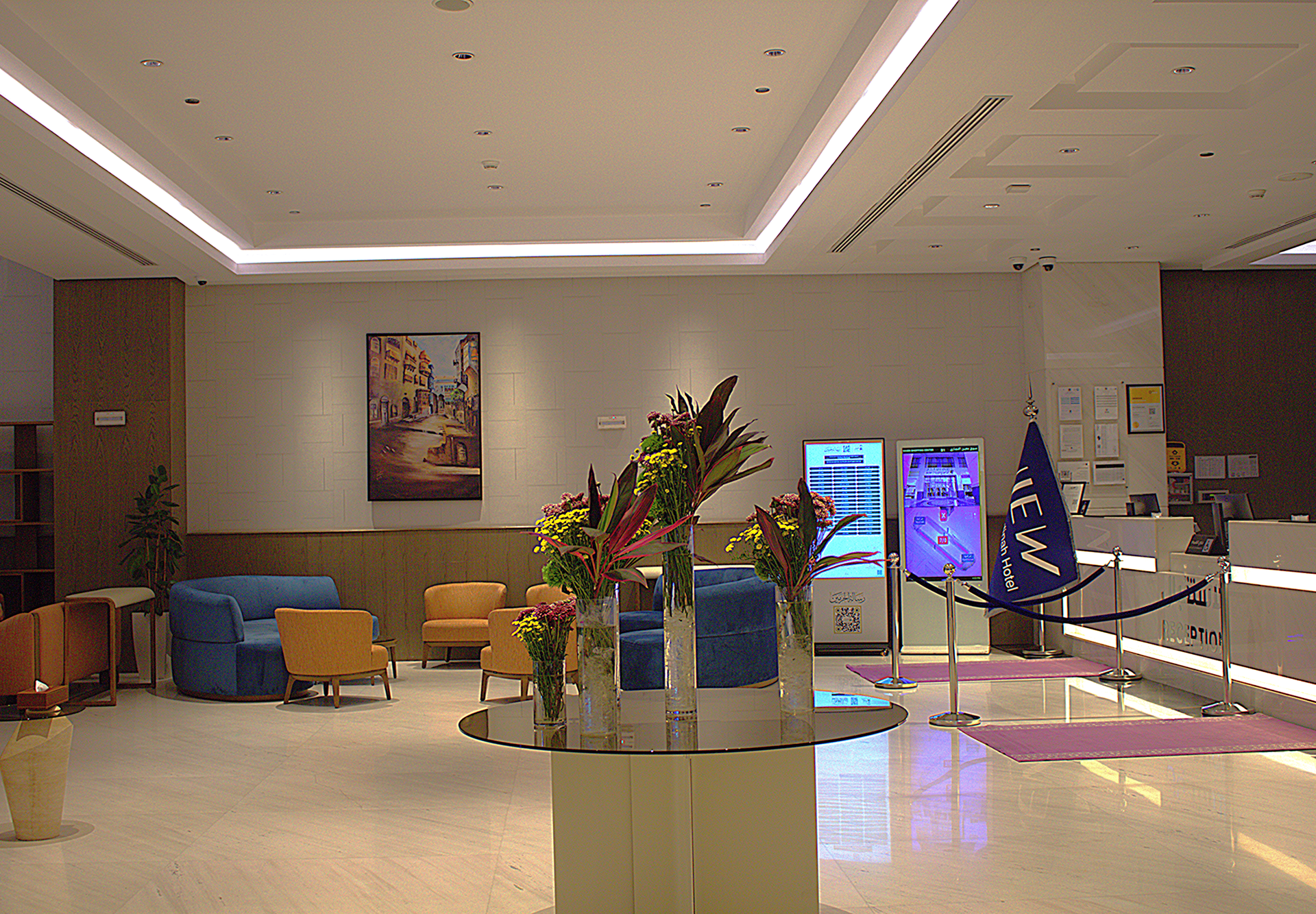 Hotel reception desk with Arabic signage, blue rope barriers, and flags in a modern lobby