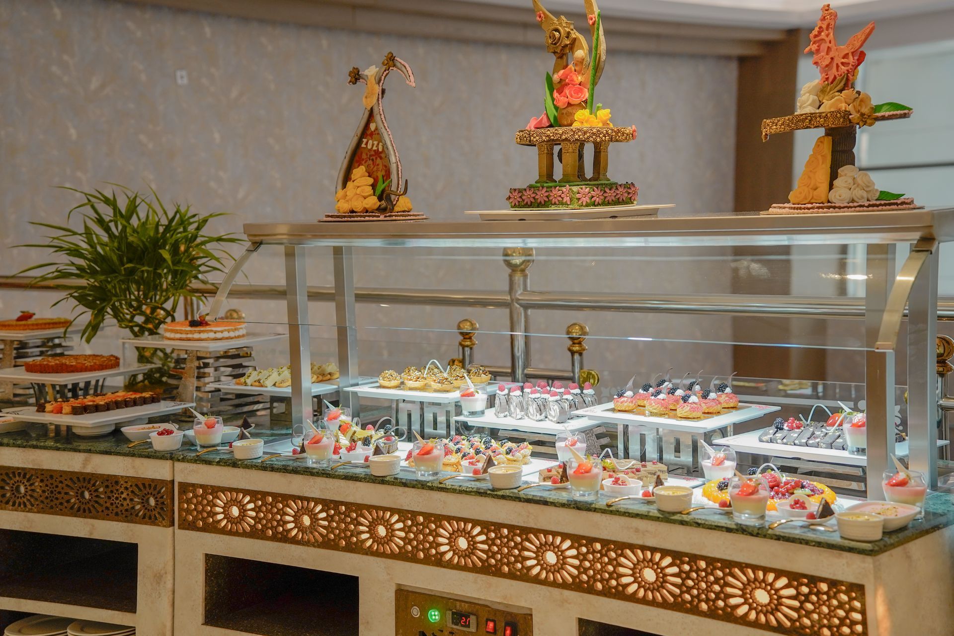 Buffet dessert display with pastries under glass, topped with decorative floral arrangements