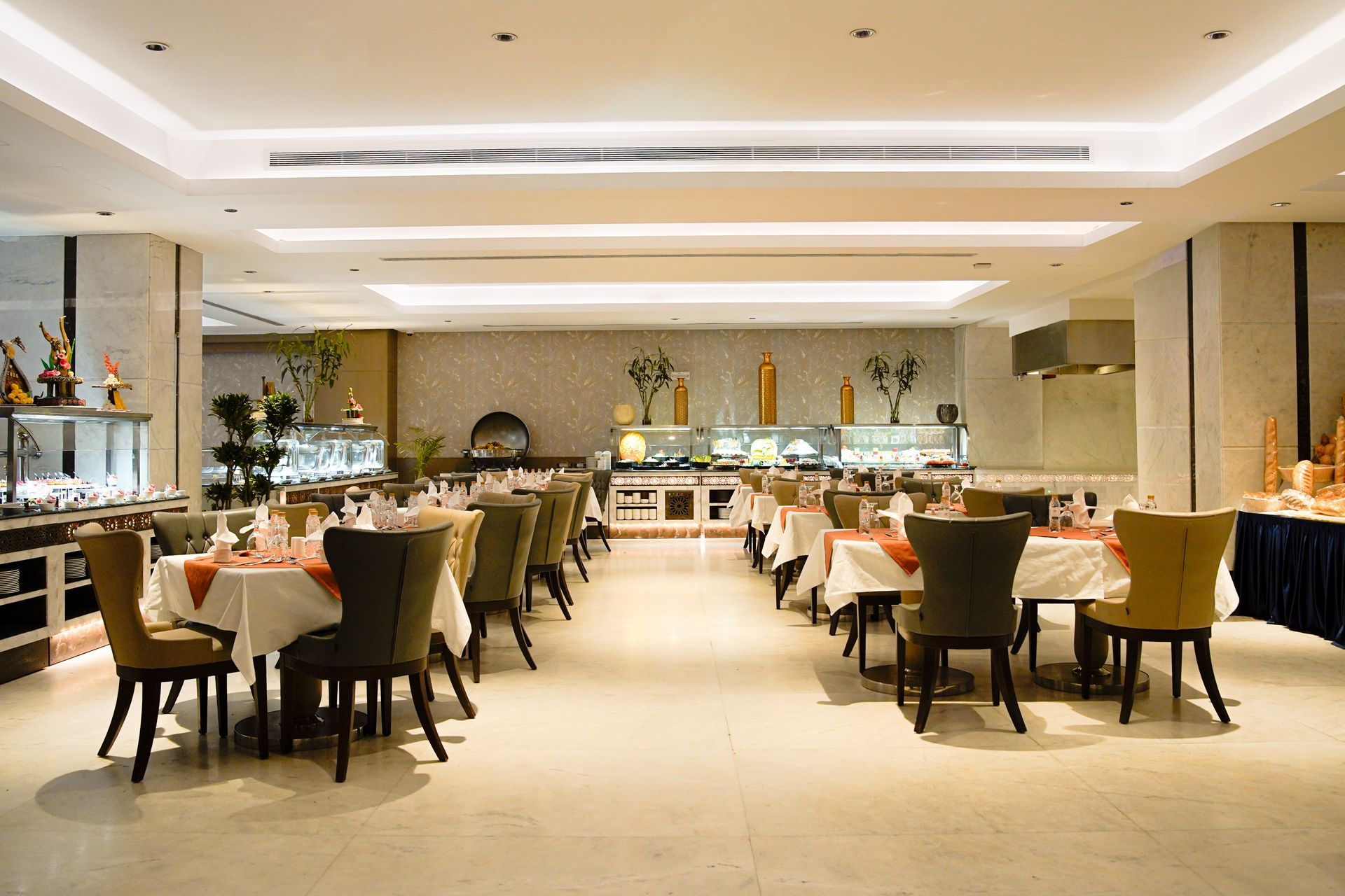 Elegant hotel dining room with set tables, upholstered chairs, and a bright buffet counter