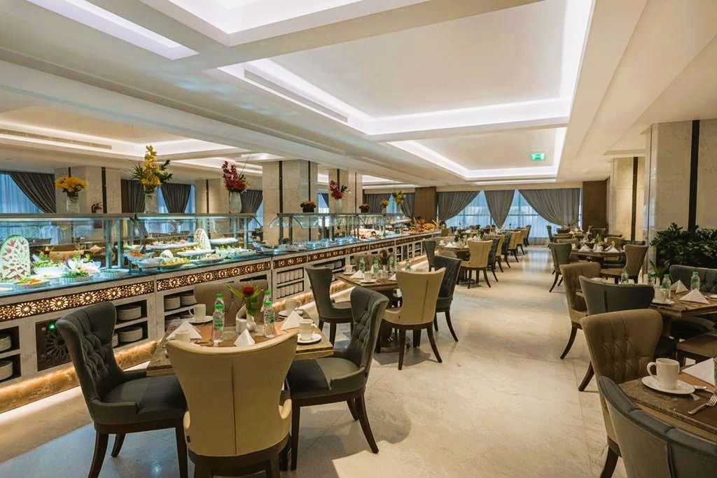 Elegant hotel restaurant with set tables, upholstered chairs, buffet counter, and bright ceiling lights