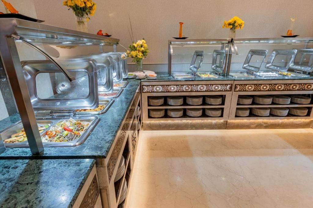 Buffet counter with stainless steel trays, glass sneeze guards, and yellow flower centerpieces in a bright dining room
