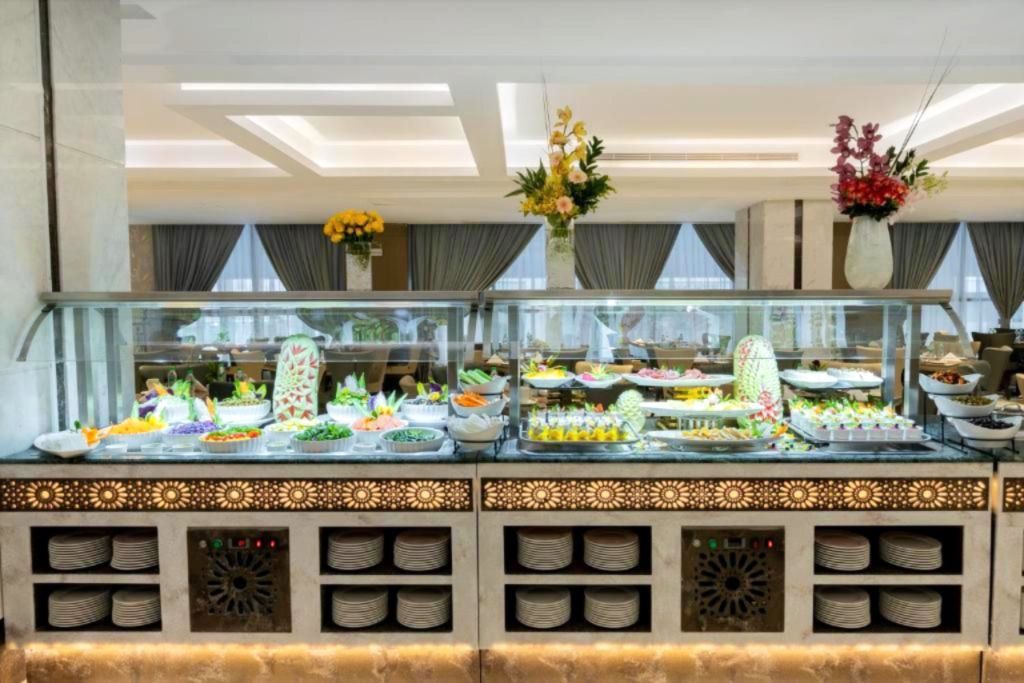 Buffet counter with covered dishes, fruit, and floral arrangements in a bright banquet hall