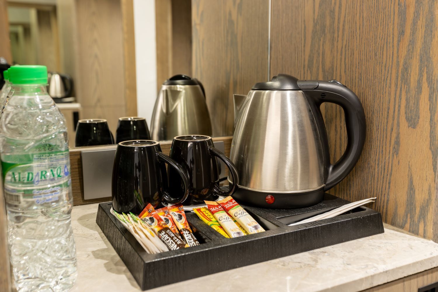 Hotel room tray with electric kettle, cups, tea, and bottled water on a countertop