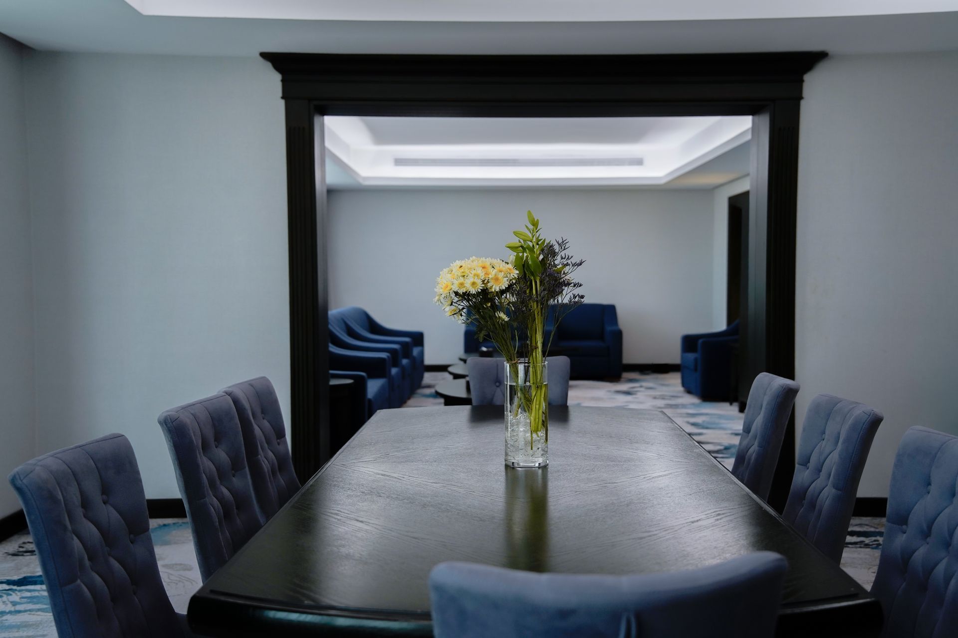 Modern dining room with a long black table, blue chairs, and a vase of yellow flowers