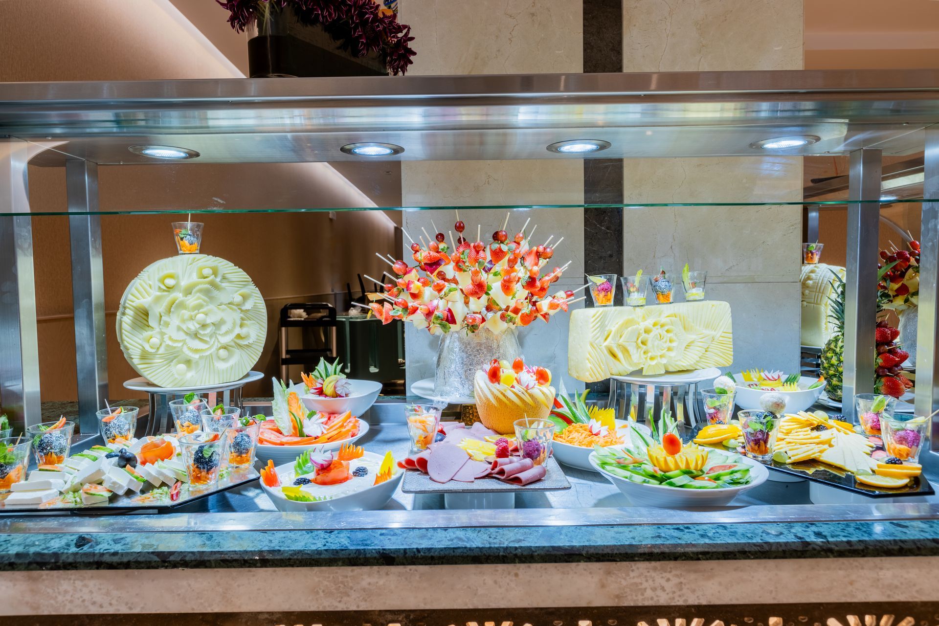 Elegant buffet dessert display with colorful pastries, cakes, and fruit on a mirrored counter