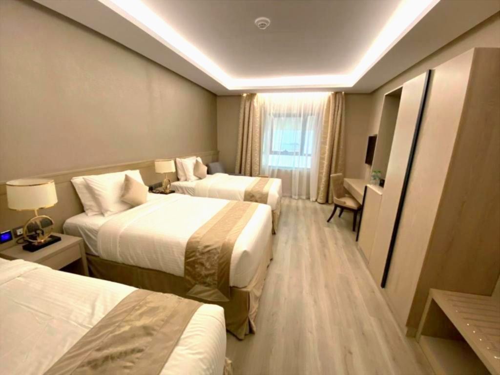 Hotel room with three neatly made beds, beige decor, and a window at the far end.