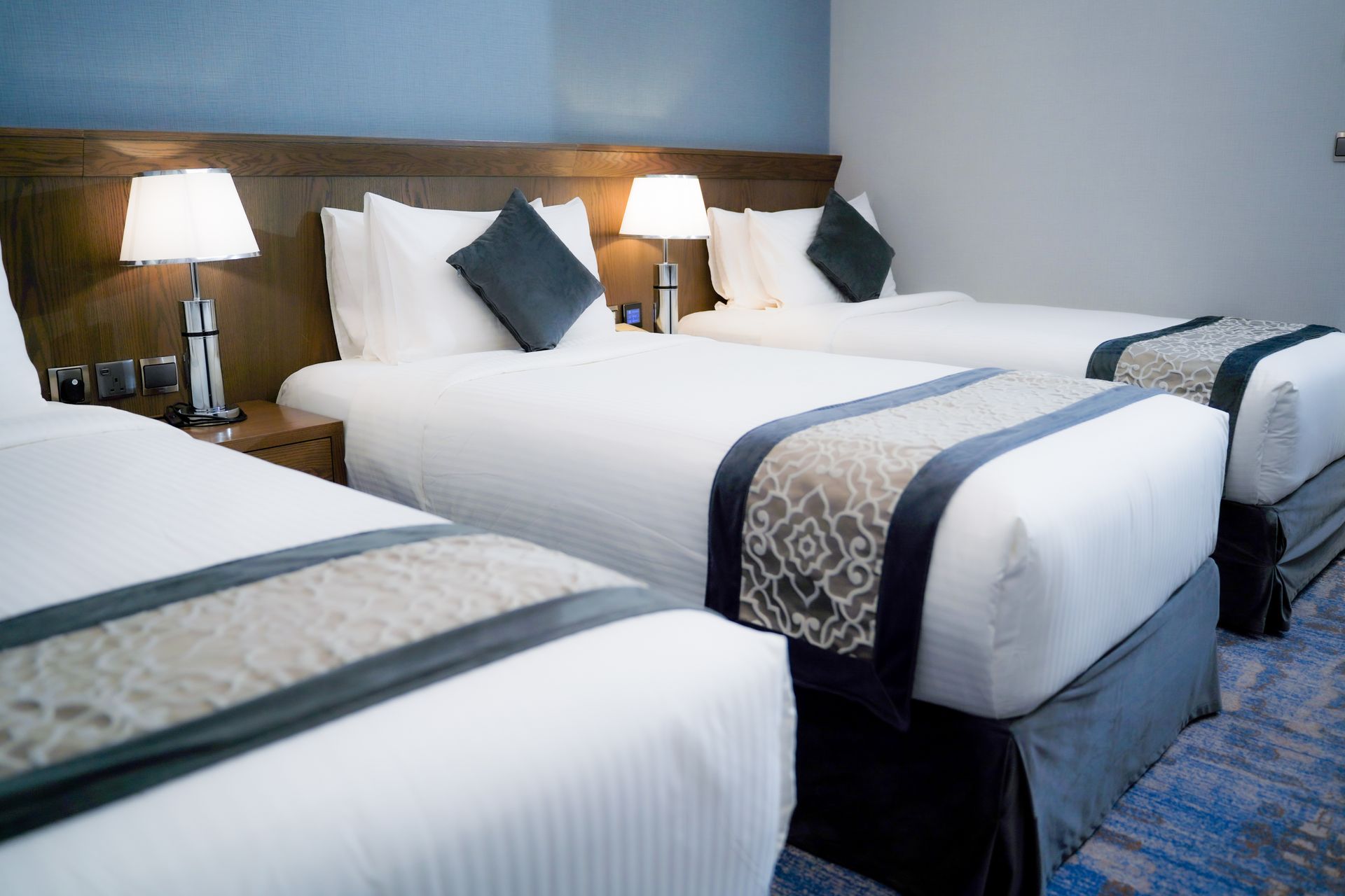 Hotel room with three neatly made beds, bedside lamps, and blue-gray decor