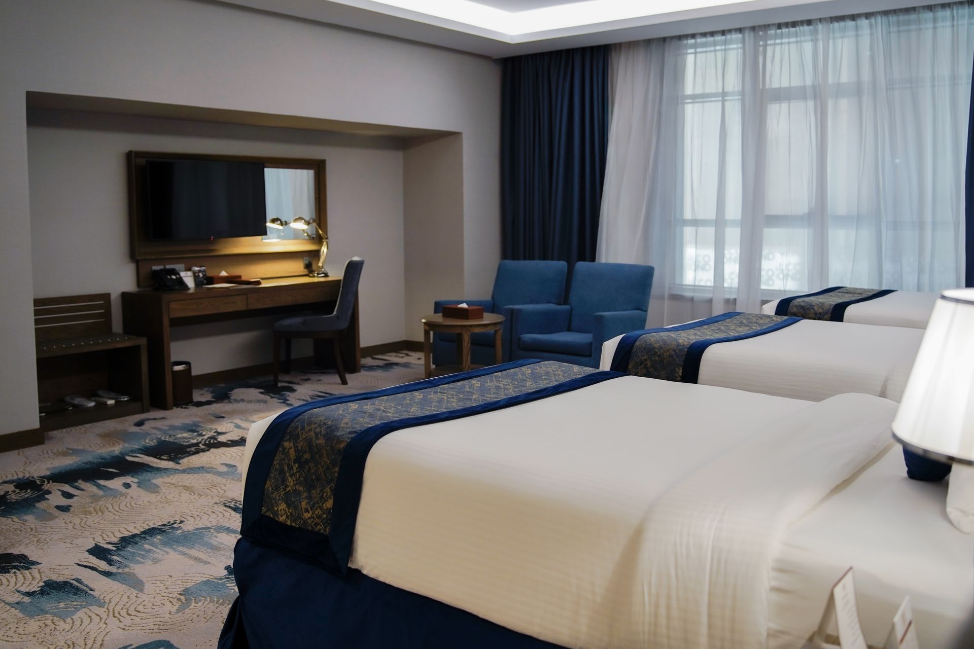 Hotel room with two beds, blue armchairs, and a desk by the window