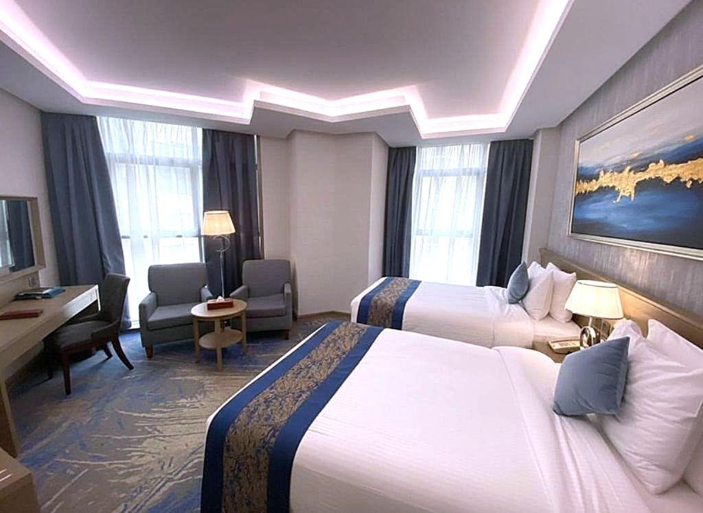 Modern hotel room with two twin beds, a gray armchair, desk, and blue-gray decor.