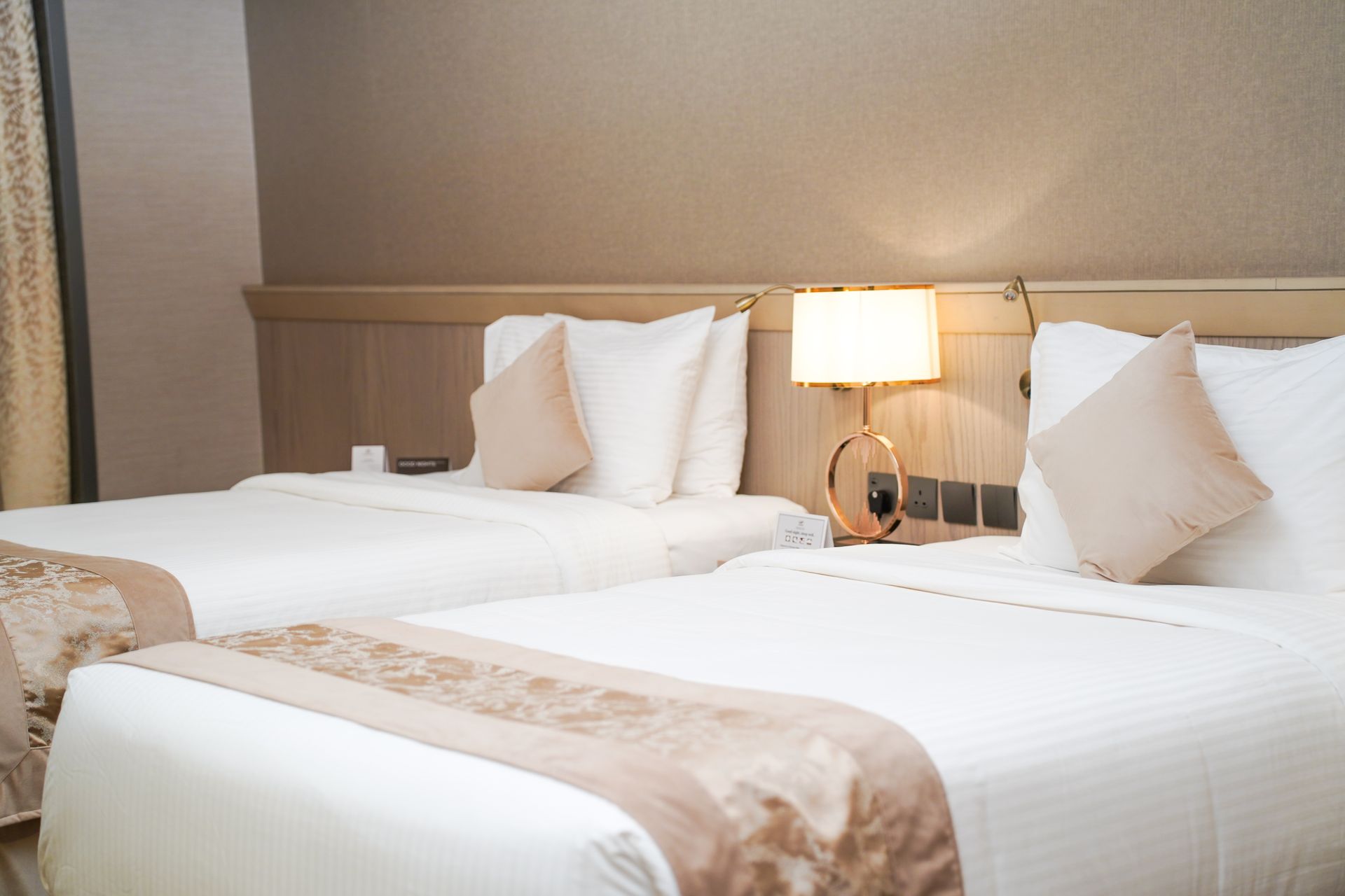 Hotel room with two neatly made twin beds and a bedside lamp between them