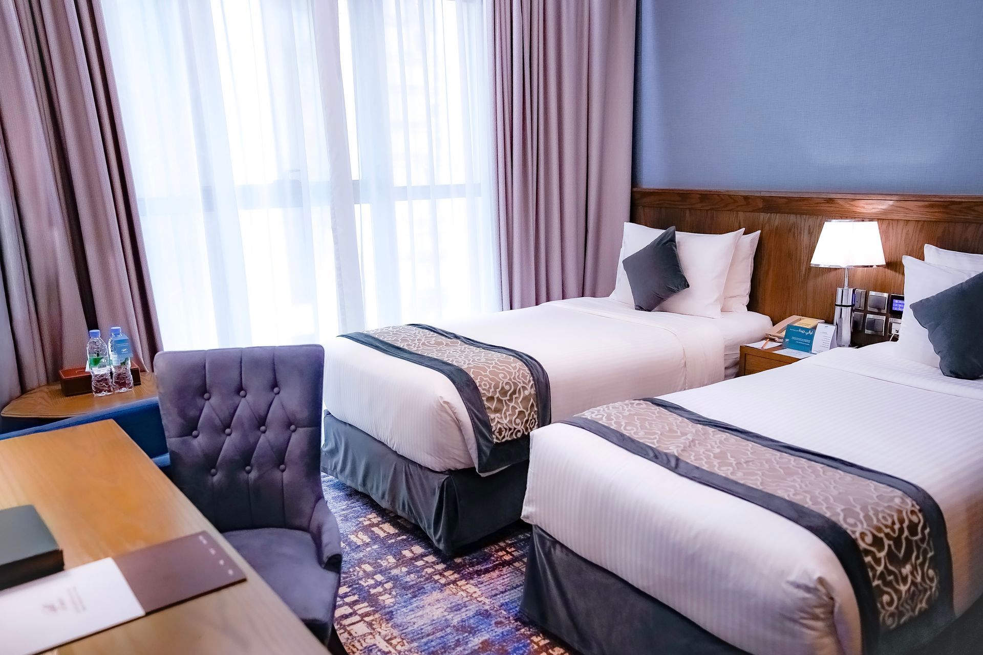 Hotel room with two twin beds, purple curtains, and a bright window