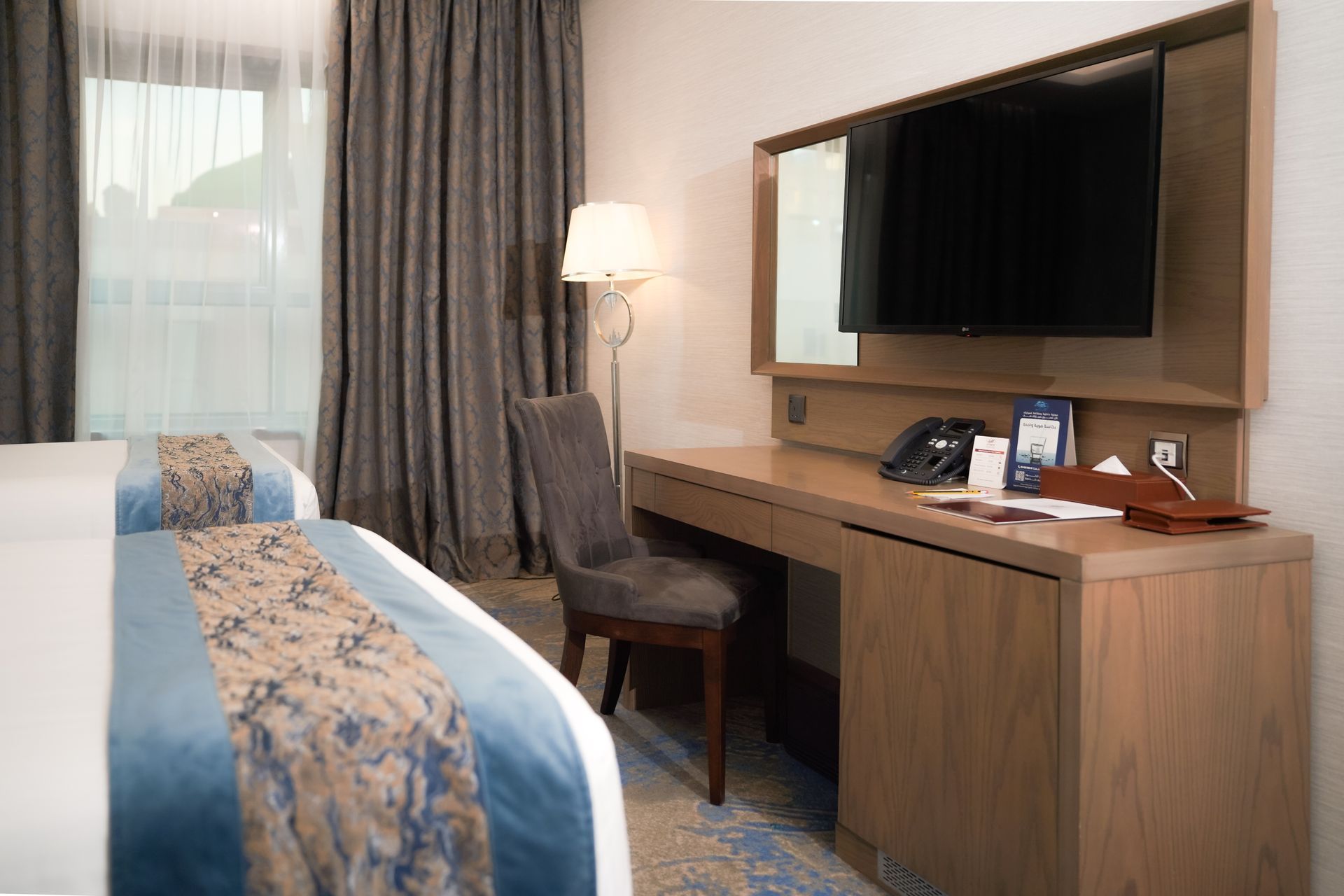 Hotel room with a bed, desk, chair, TV, lamp, and window with curtains