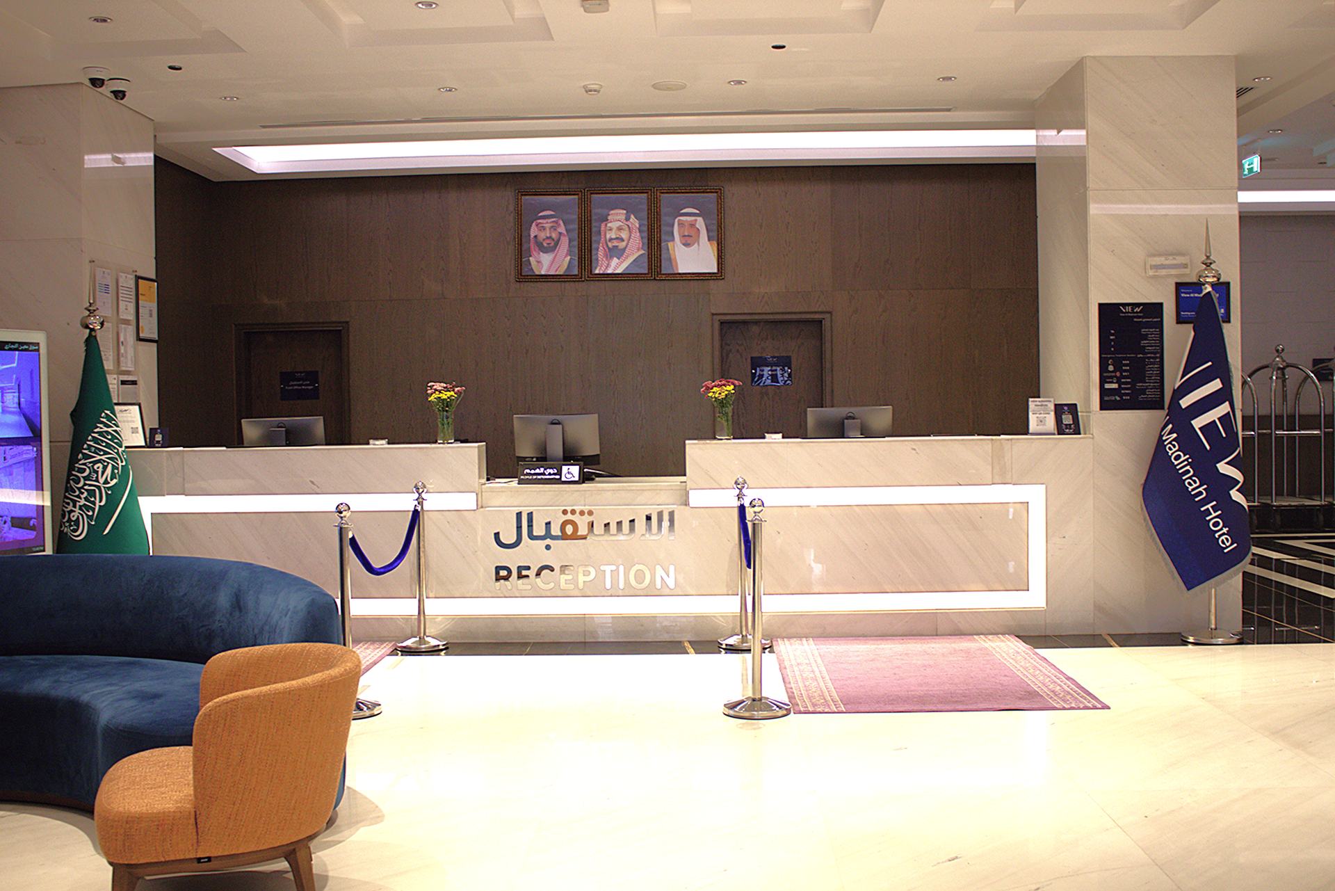 Hotel reception desk with blue velvet ropes, flags, and wall portraits in a modern lobby