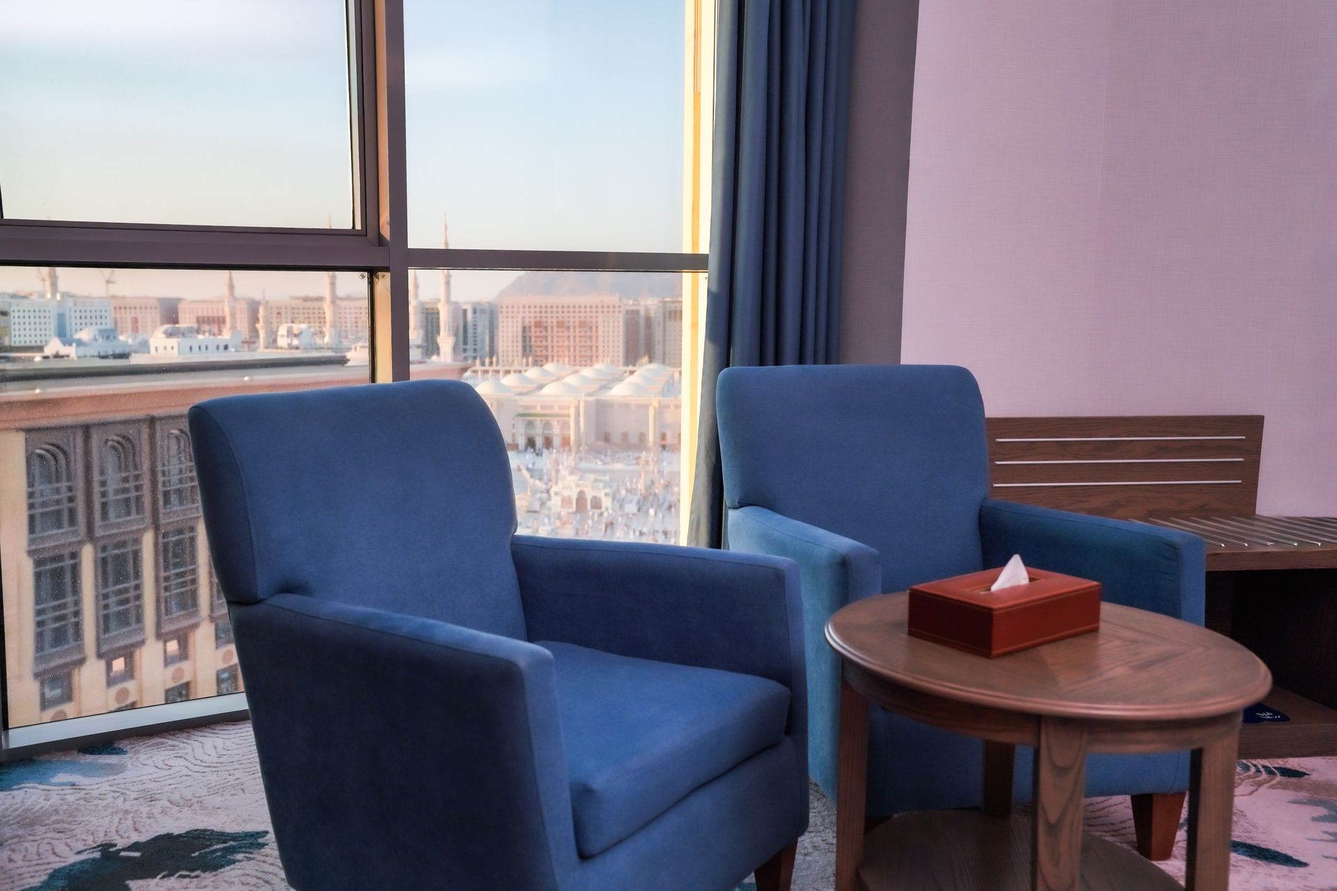 Blue chairs beside a small table by a large window overlooking city buildings