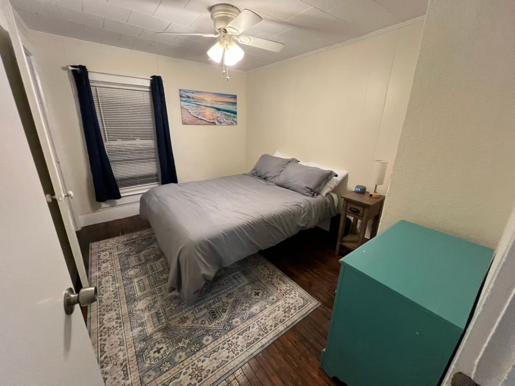 A bedroom with a bed , nightstand , rug and ceiling fan.