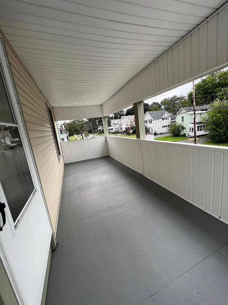 A large porch with a gray floor and a white railing.