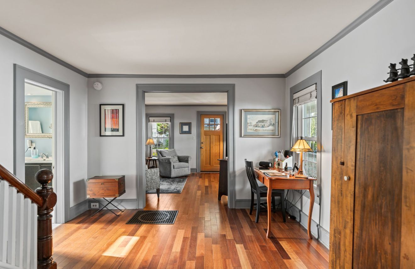 White two-story house with a front porch, American flag, and landscaped yard on a sunny day.