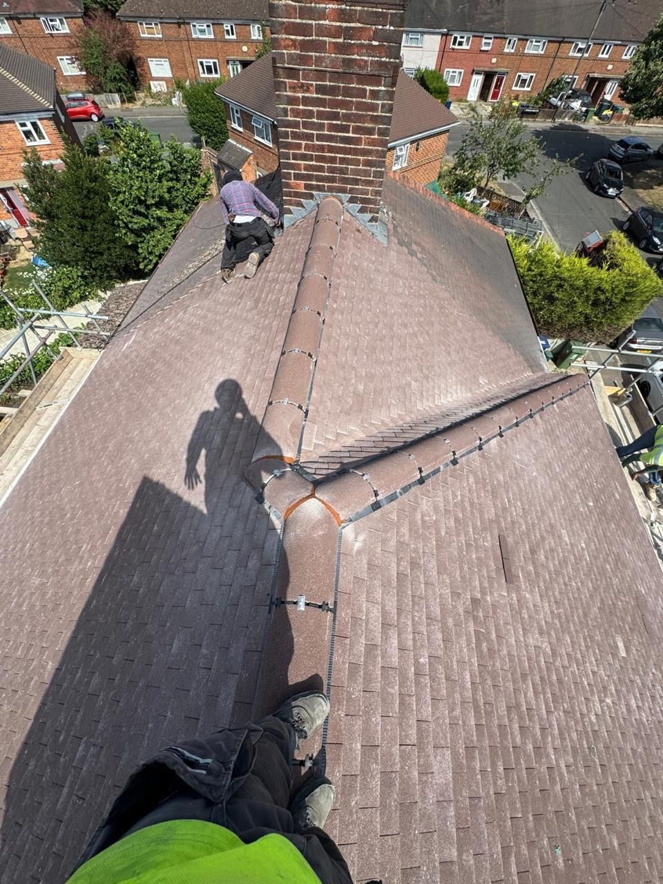 High-angle view of two roofers working on a tiled roof near a brick chimney on a sunny day.