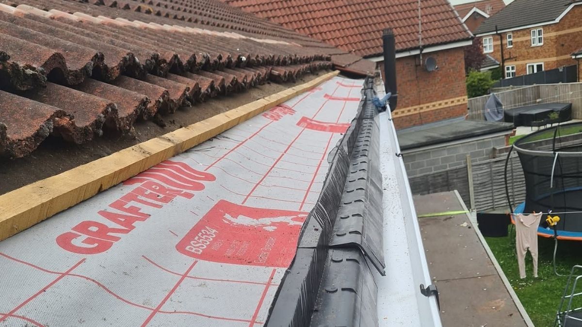 Dark grey resin driveway leading to a white garage door, flanked by gardens with greenery.