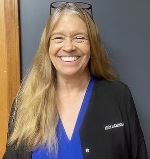 A woman wearing glasses and a blue shirt is smiling for the camera.