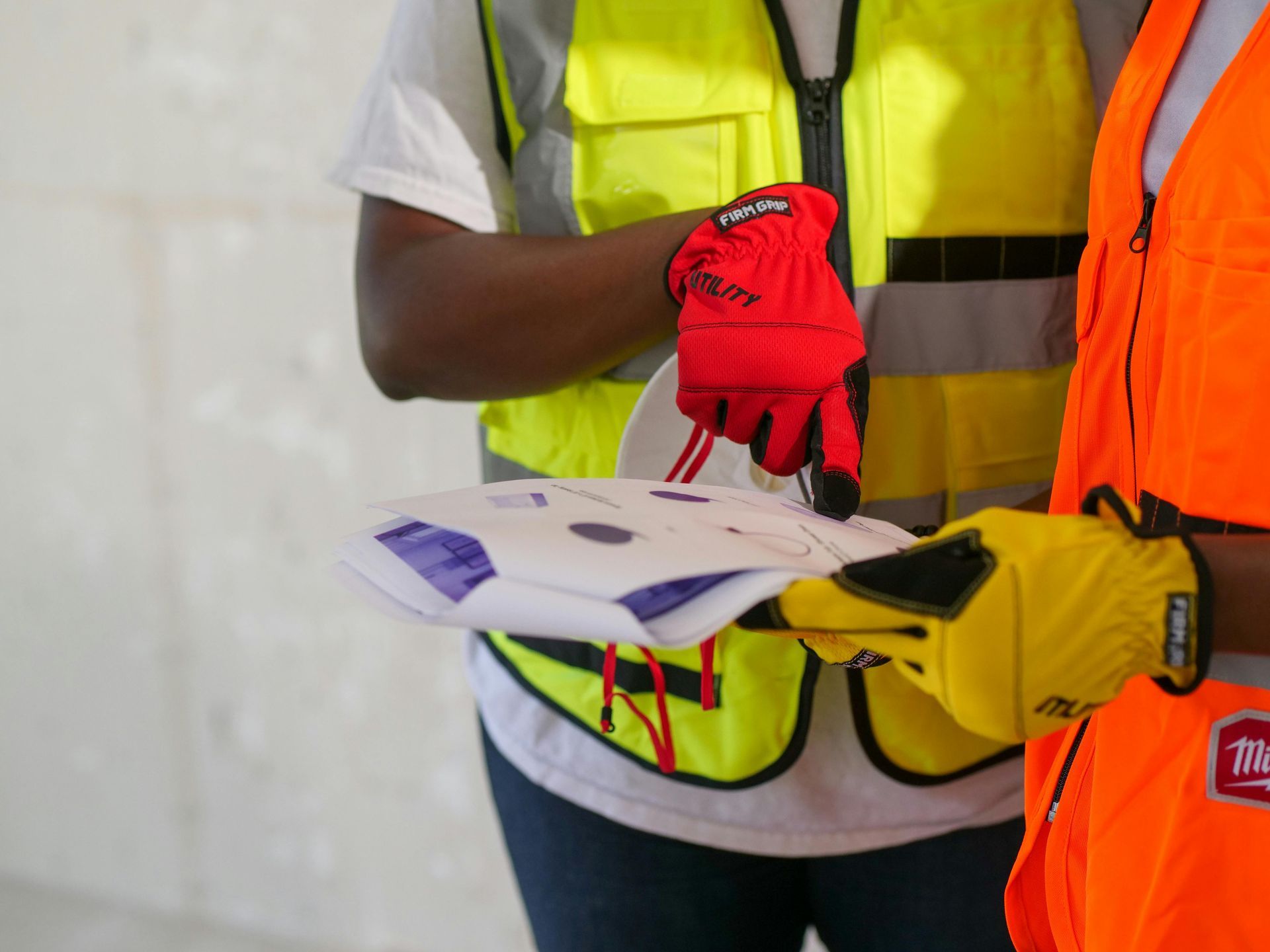 Two people wearing safety vests and gloves are looking at a piece of paper