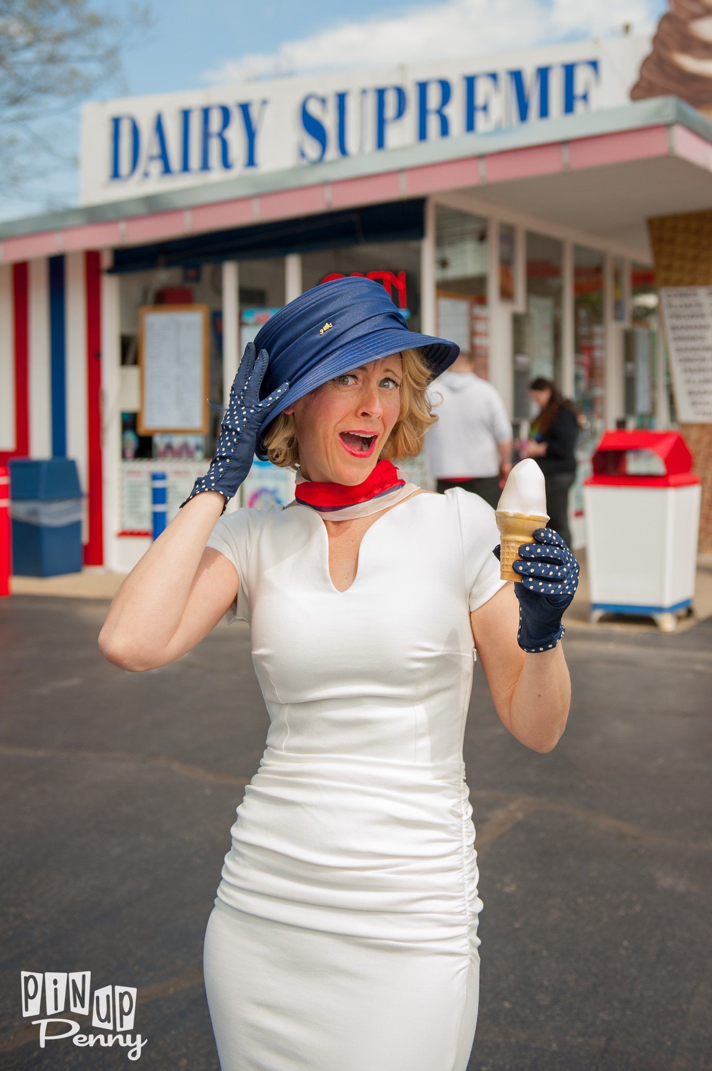 a woman in a white dress is holding an ice cream cone in front of a dairy supreme store .